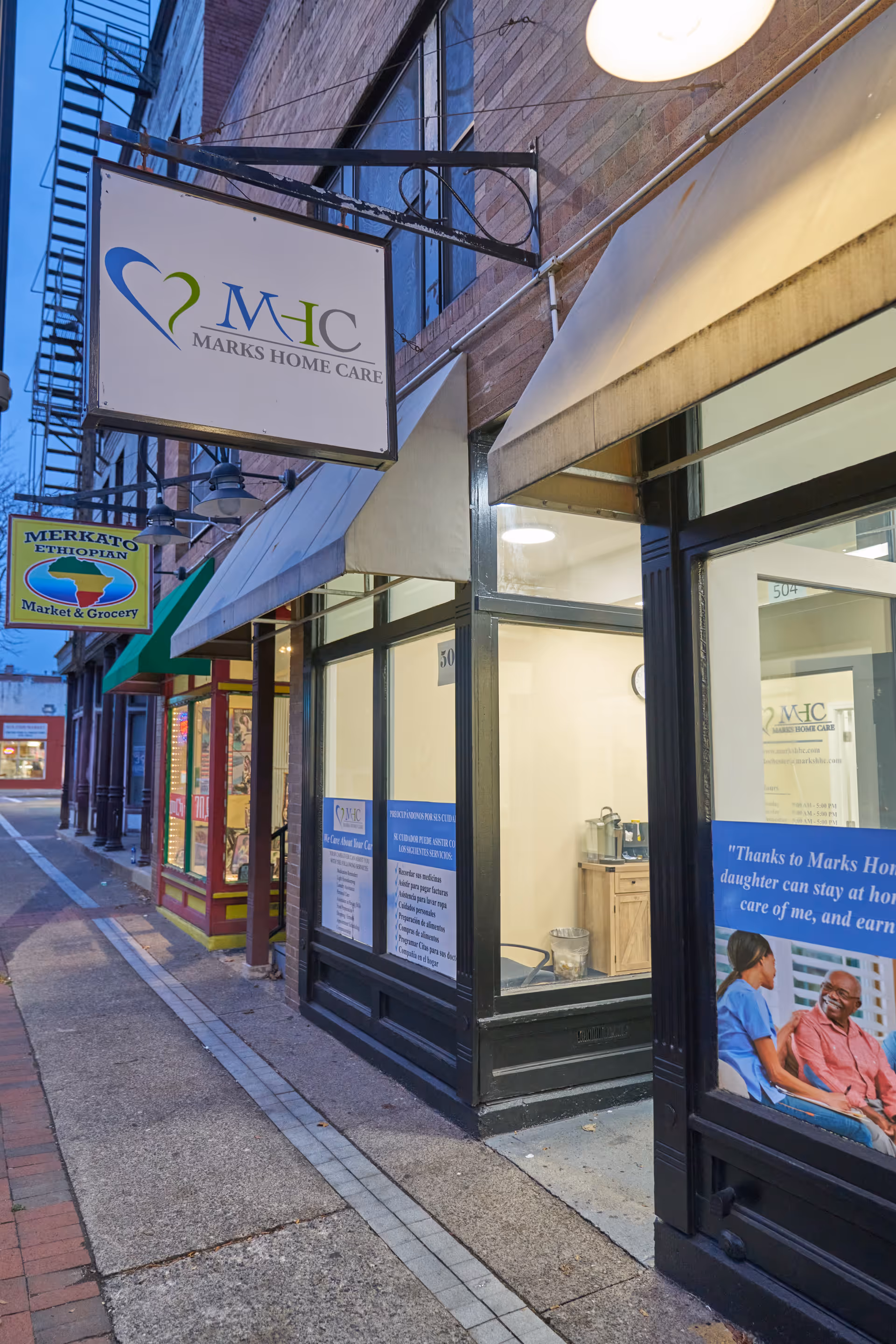 Exterior storefronts along a city street display a Marks Home Care Agency Rochester sign.