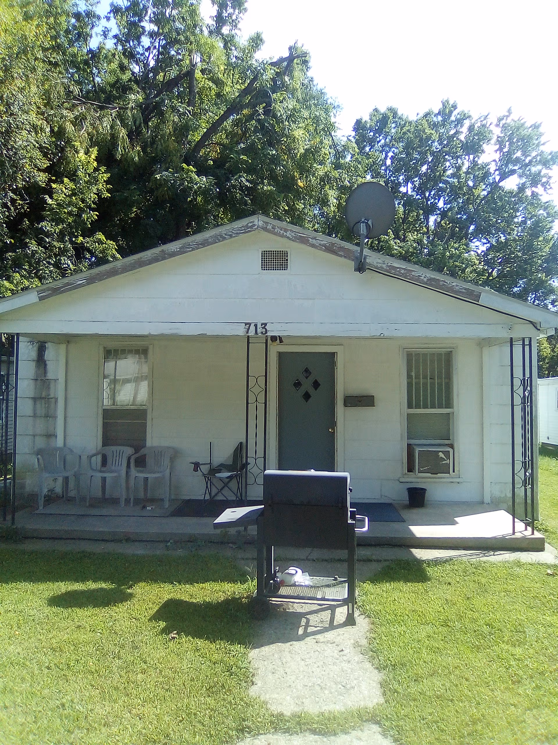 Small single-story front of a house-like building with a porch and chairs.