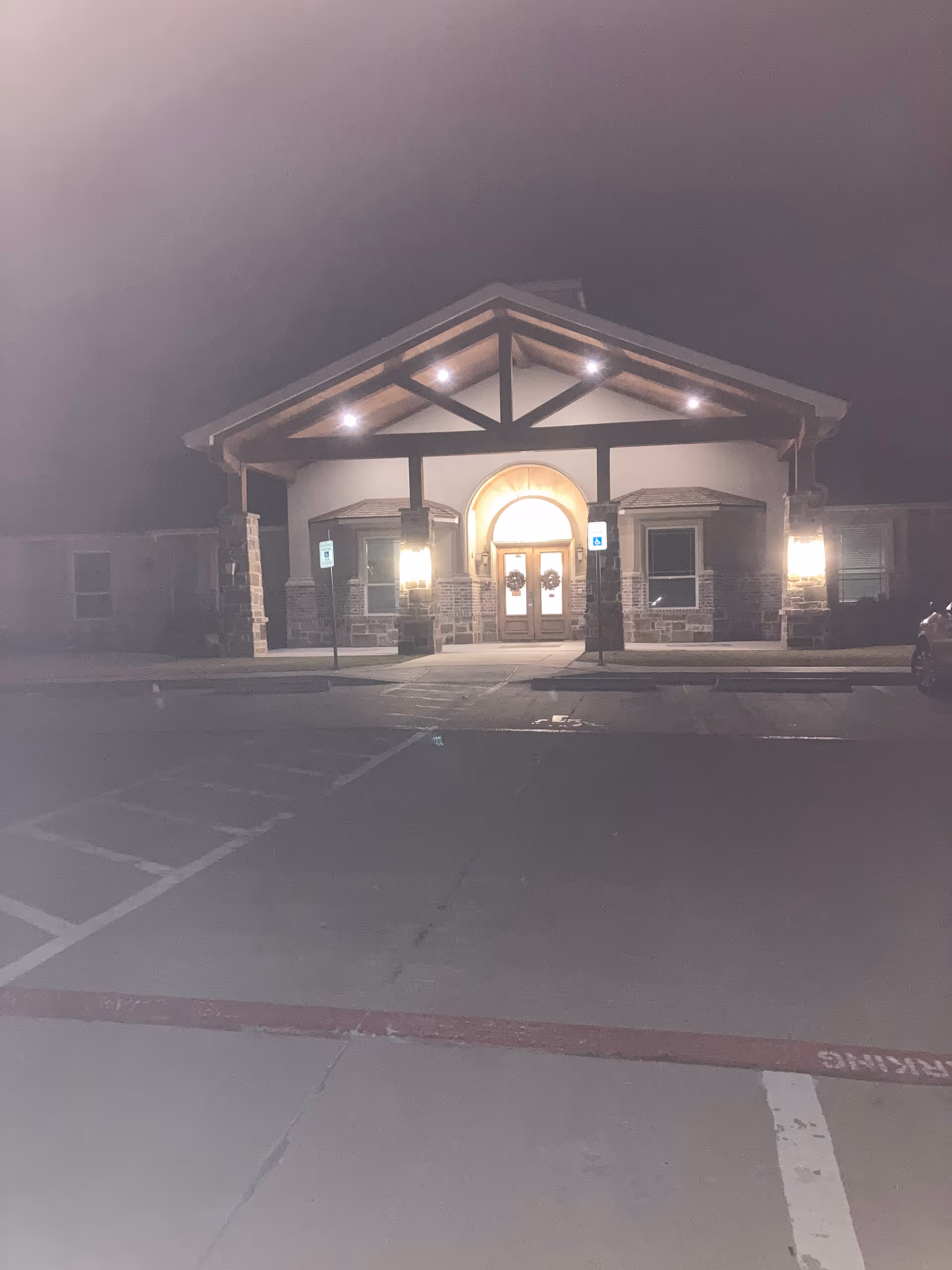 Night view of a memory care community entrance with illuminated arch and handicap parking.