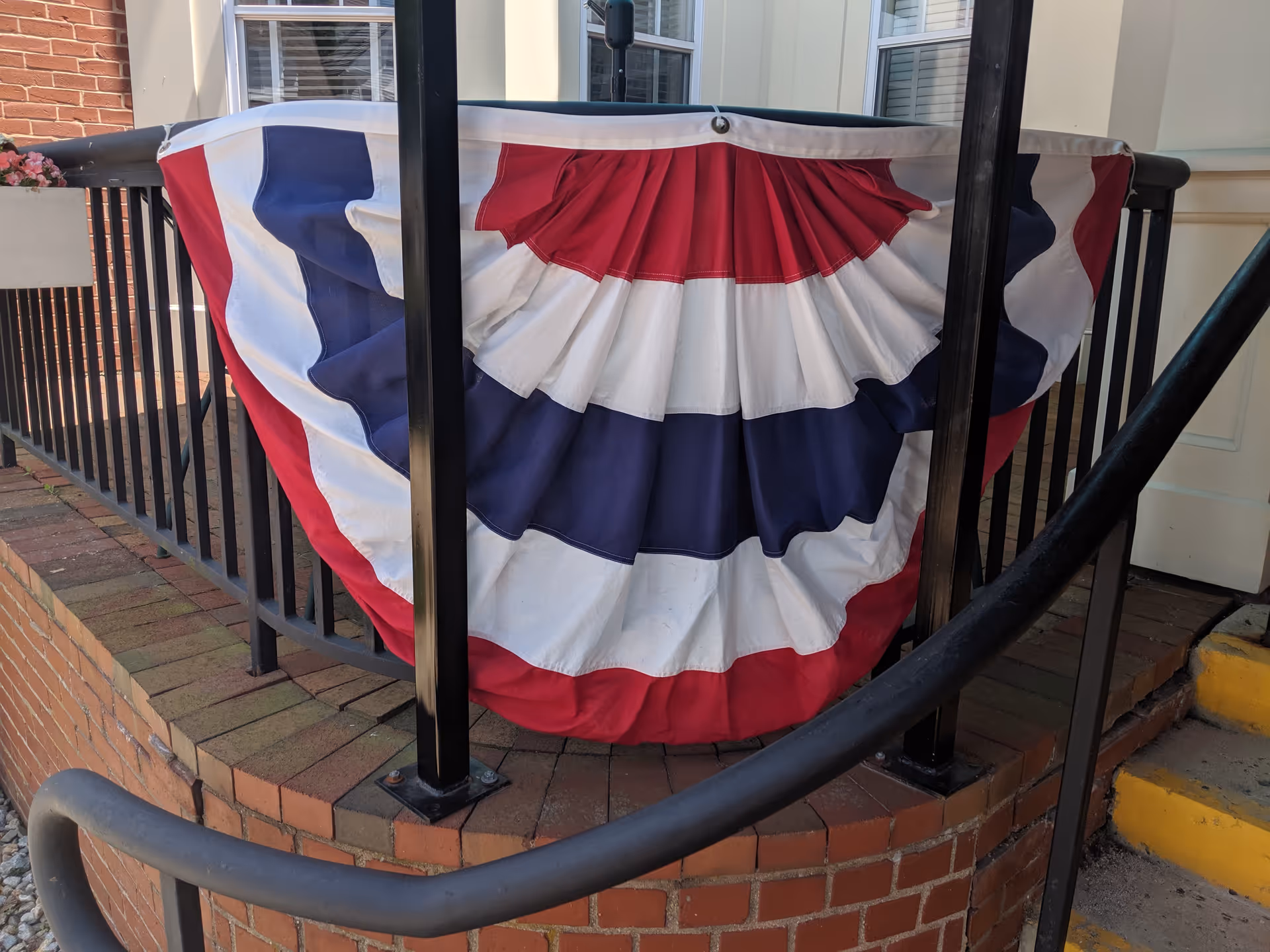 Patriotic bunting in red, white, and blue is draped over a railing near a brick entrance.