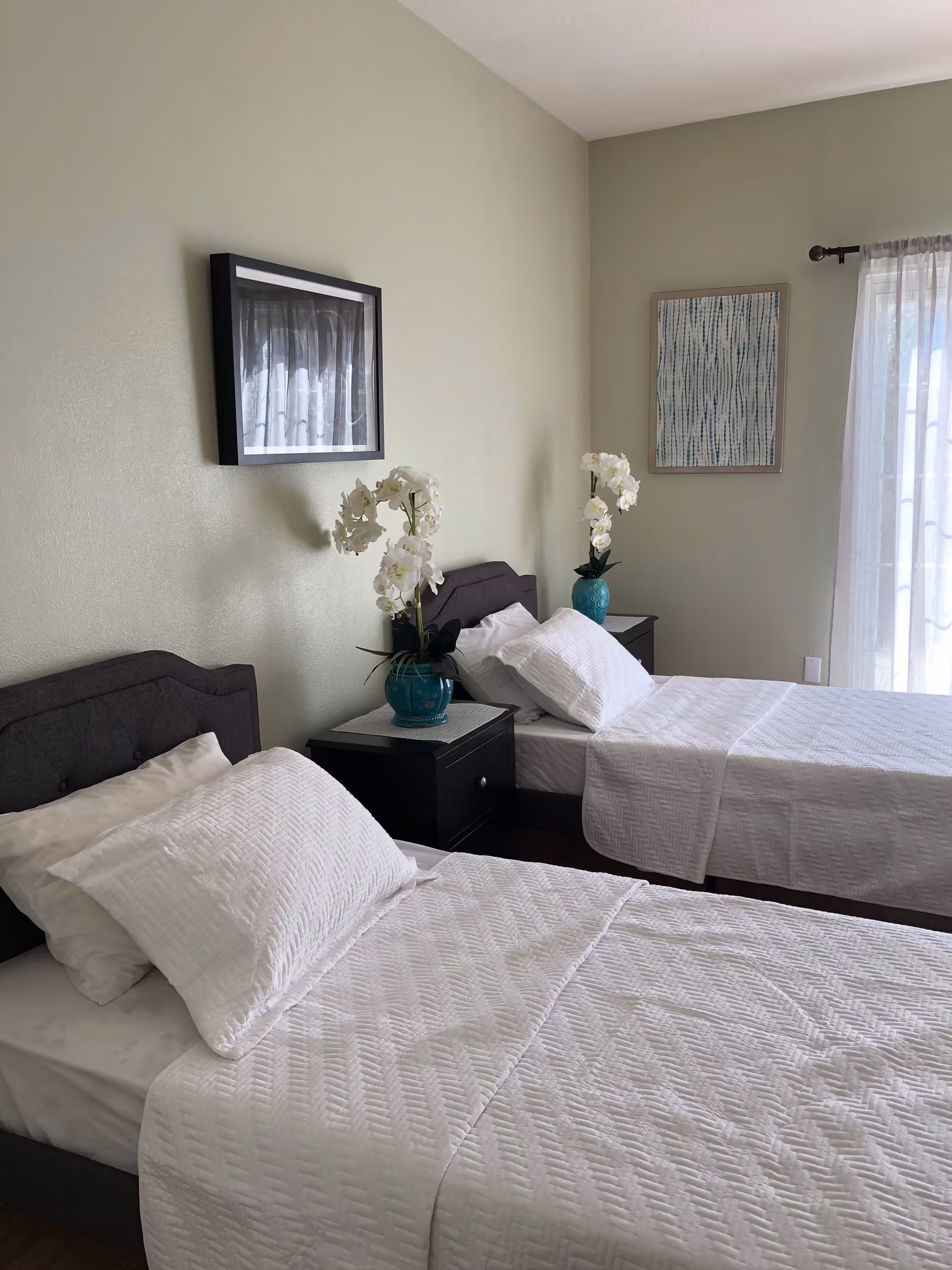 Two twin beds with white bedding and teal vases in a shared bedroom.