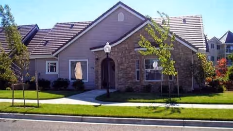 Single-story senior living facility with a stone facade, manicured lawn, and curved walkway.