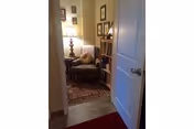 Cozy living area in an apartment with chair, lamp, bookshelf, and framed photos beside a doorway.