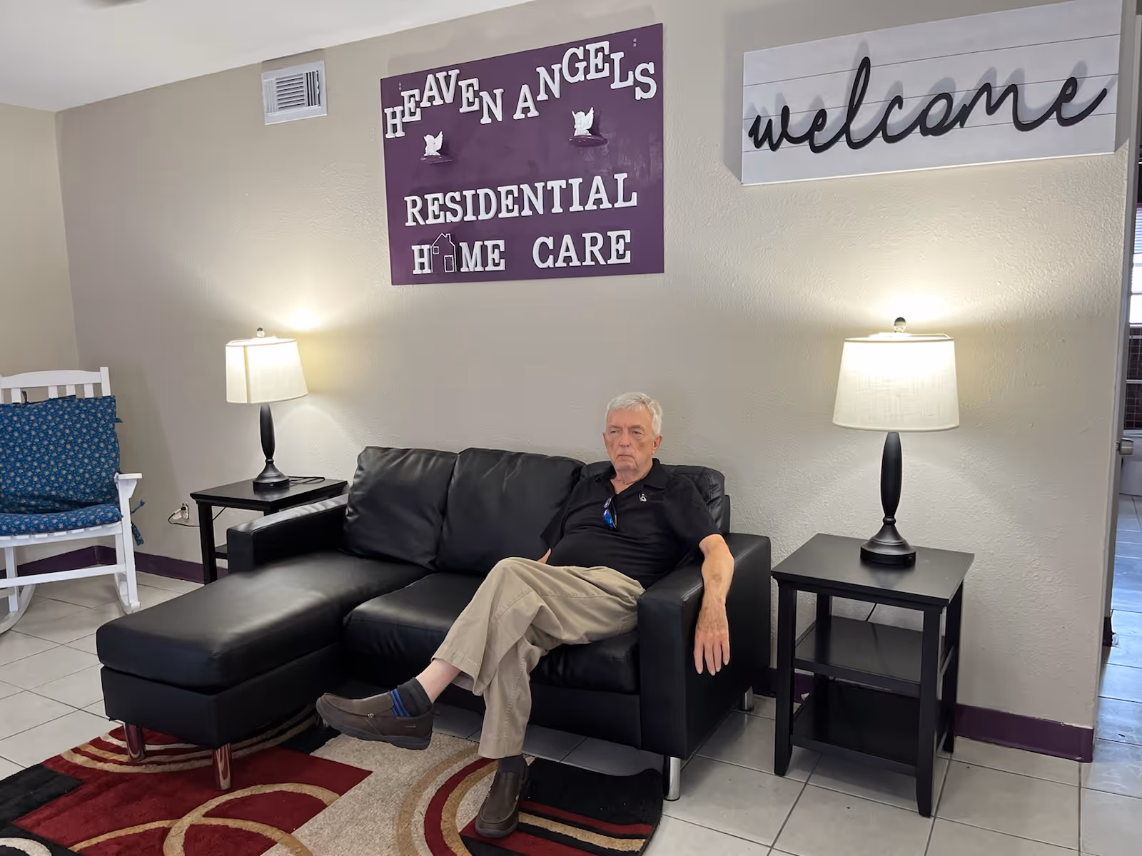 Older man seated on a black leather sofa in a lounge with Heaven Angels signage.