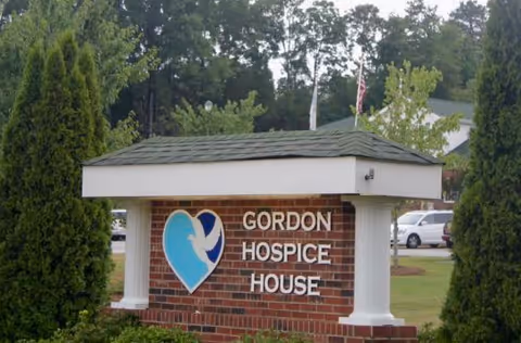Brick sign with a blue heart logo reading Gordon Hospice House among trees.