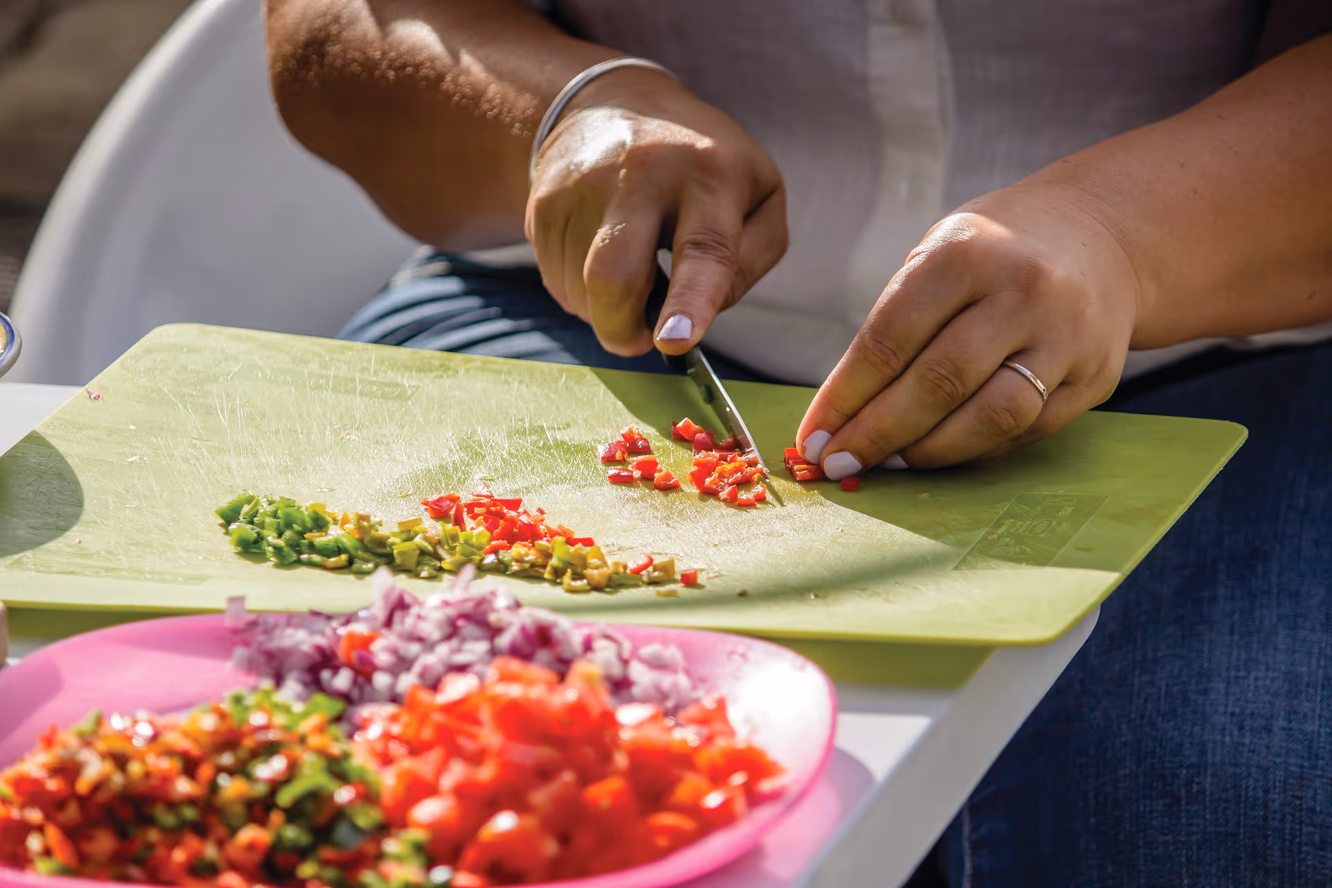 A person chops red and green peppers on a green cutting board beside a pink plate.