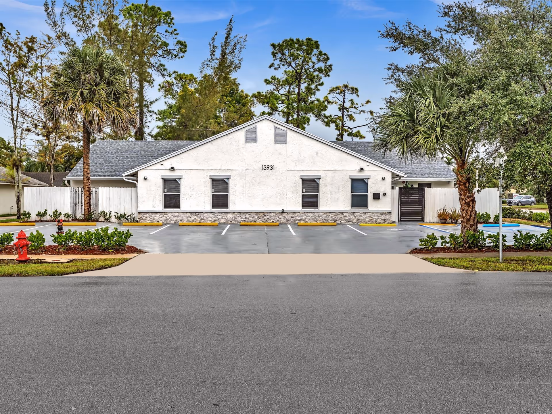 Front view of a white single-story assisted living facility with palm trees and parking.