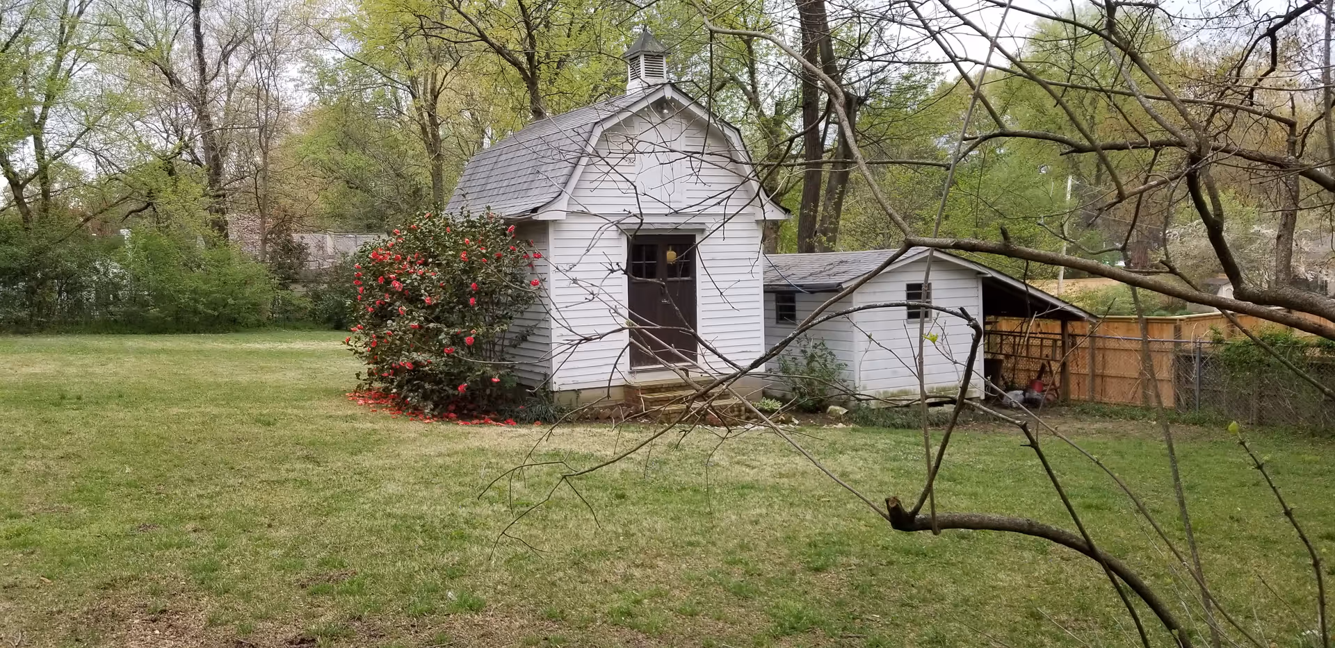 Small white shed and outbuilding in a grassy yard with trees.