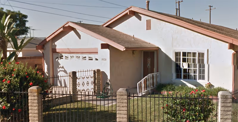 Single-story residential front of Evergreen Haven with a gate, bushes, and a driveway.