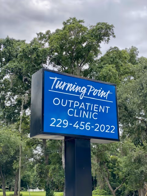 Blue Turning Point Outpatient Clinic sign on a post with trees in background.