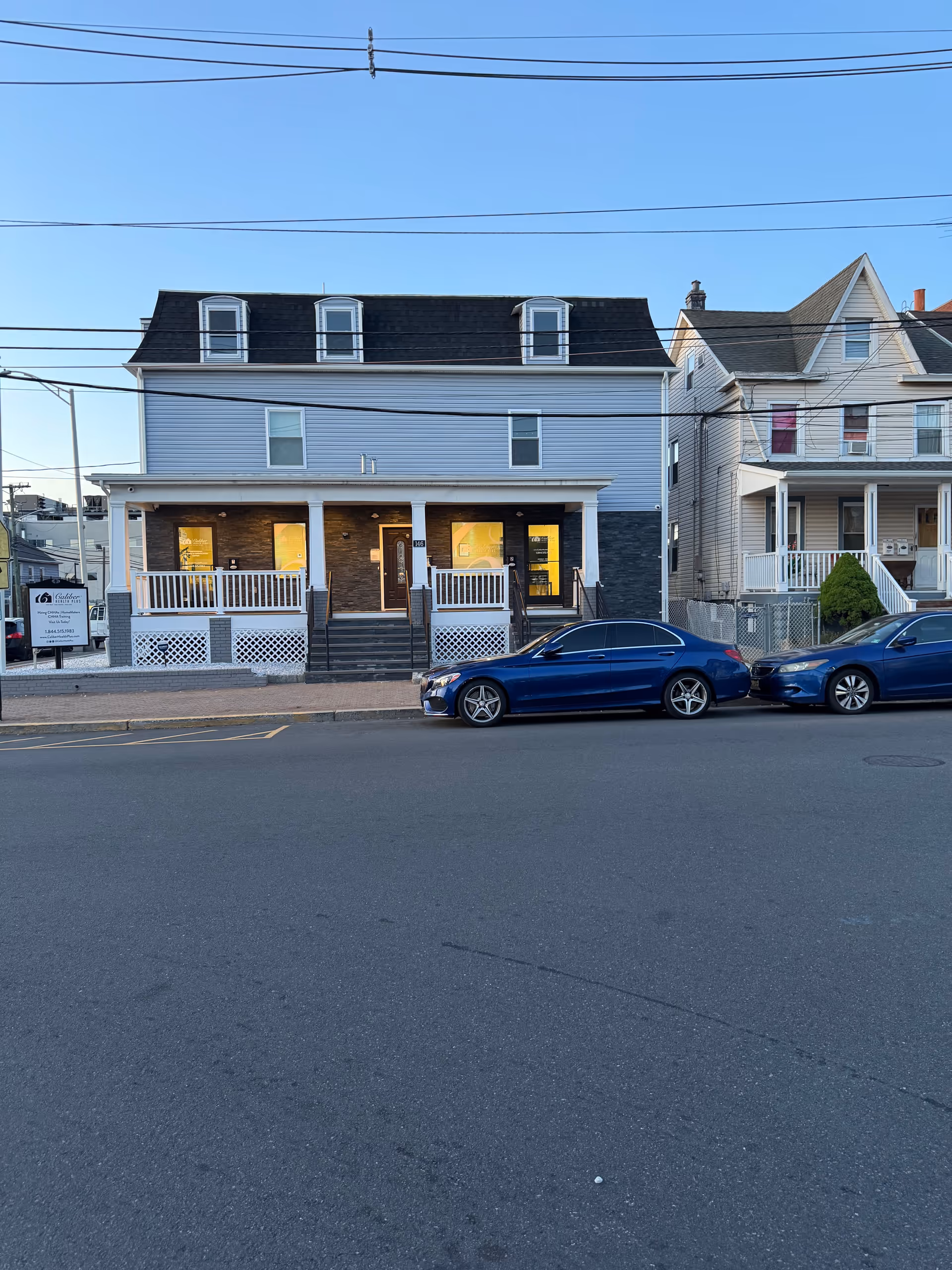 Two-story storefront-style building with a front porch and parked cars along the street.