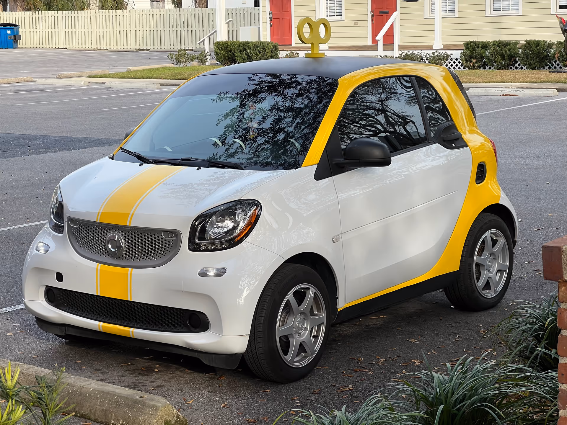 A small white and yellow car parked in a lot with residential buildings in the background.