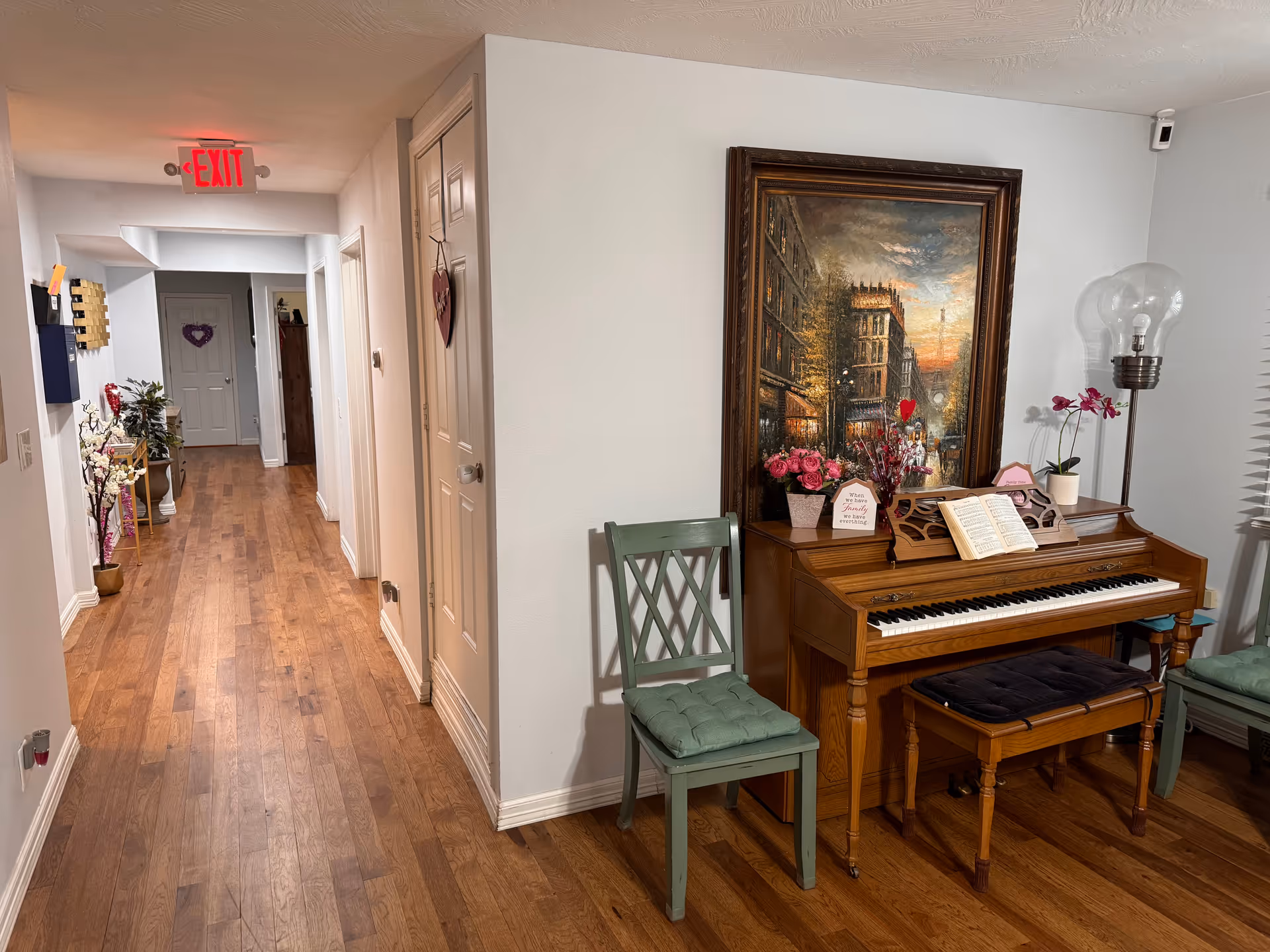 A hallway with wood floors, pastel walls, and a piano with bench beside a framed painting.