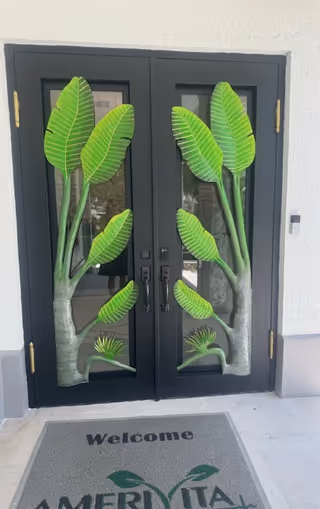 Double glass doors with tropical leaf designs and a welcome mat at entrance.