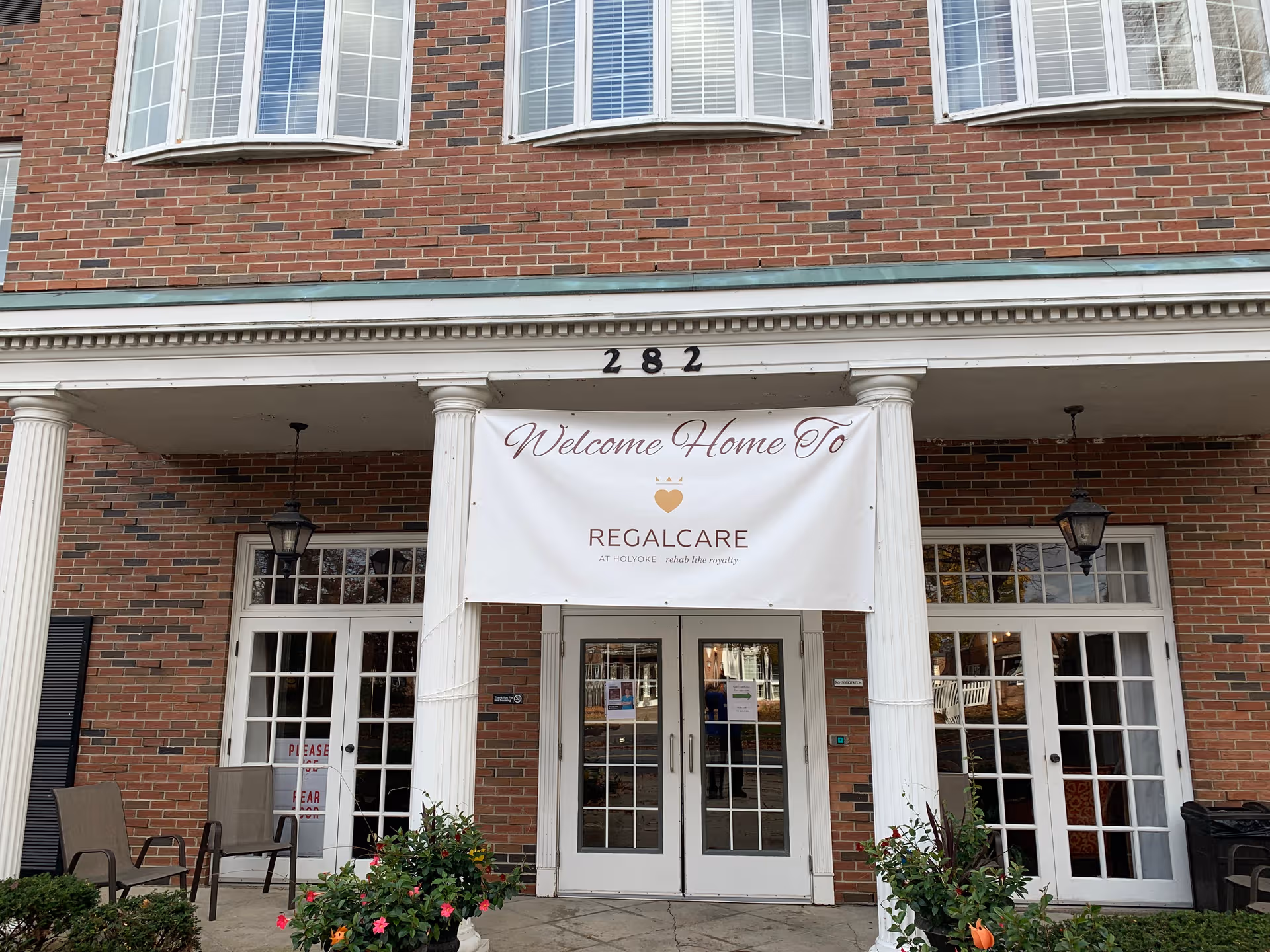 Brick building entrance with white columns and a banner reading Welcome Home To RegalCare at Holyoke.