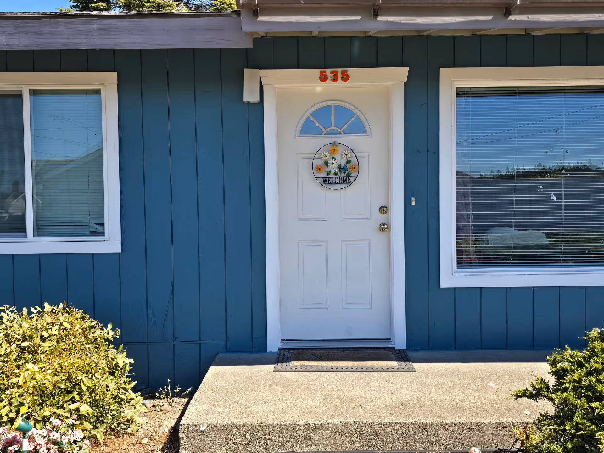 Blue building exterior with white front door and welcome wreath at the entrance.