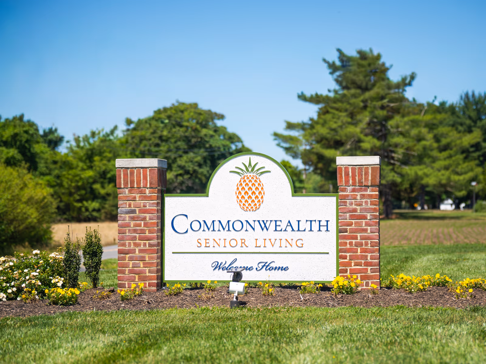 Brick entrance sign reads Commonwealth Senior Living at Farnham with pineapple emblem, set on lawn.