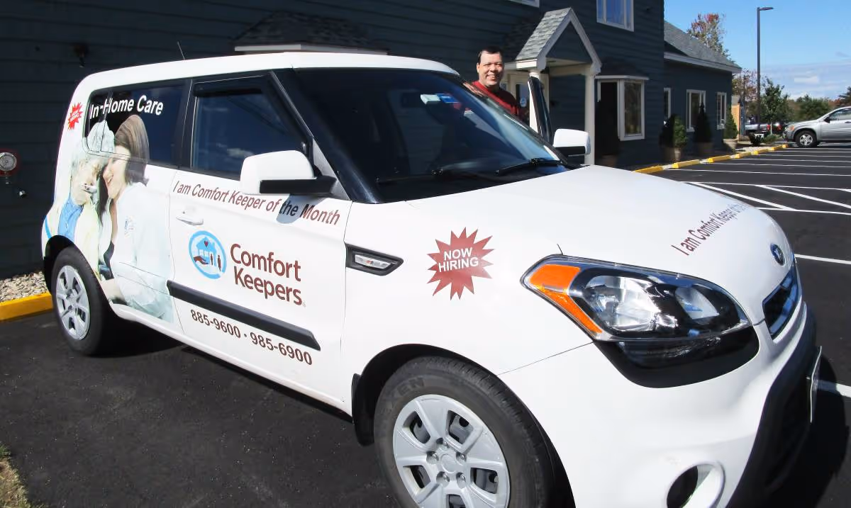 White Comfort Keepers van parked outside a blue building, with a person by the open door.
