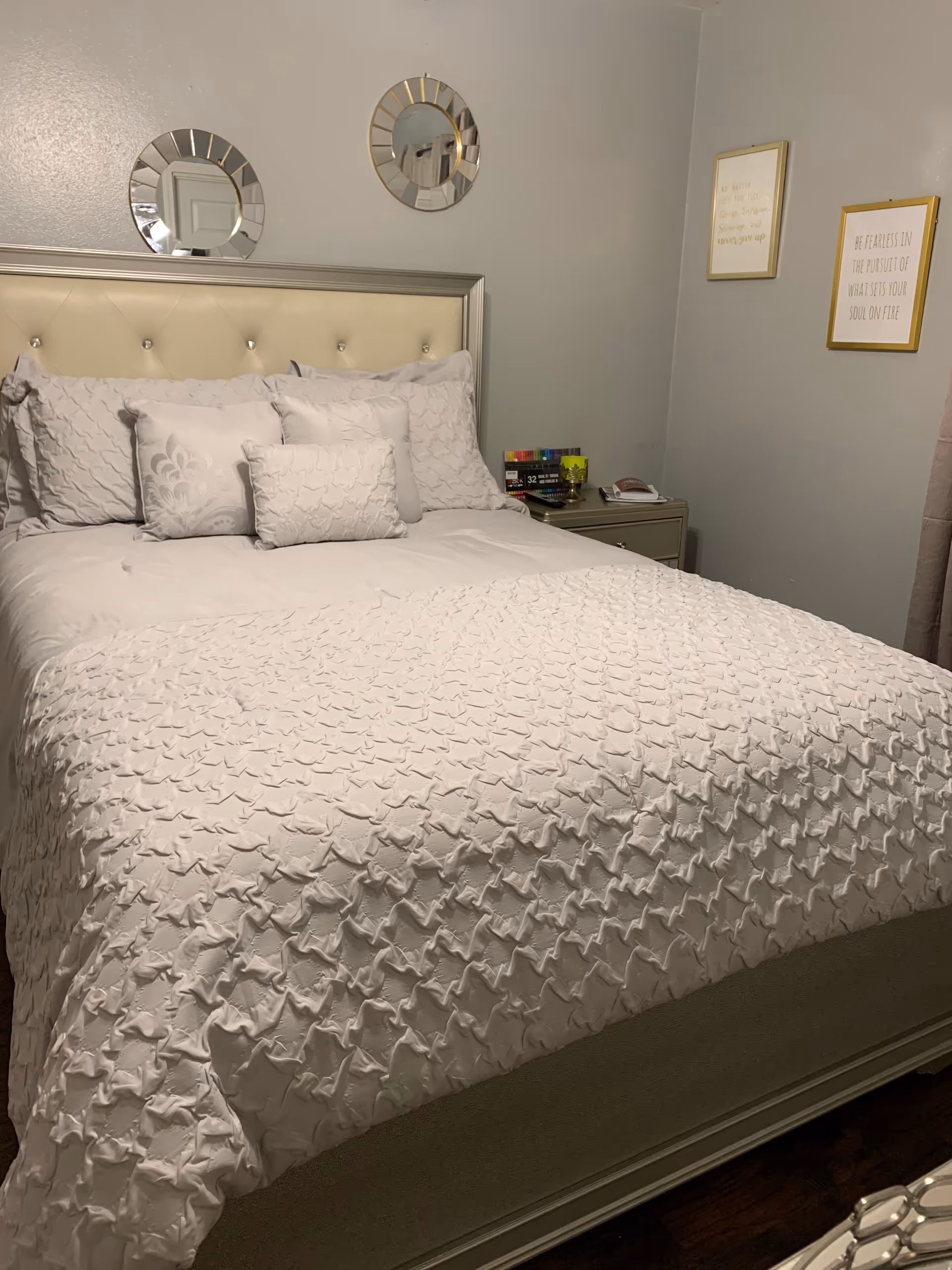 A neatly made bedroom with a tufted headboard, white bedding, and wall decor.