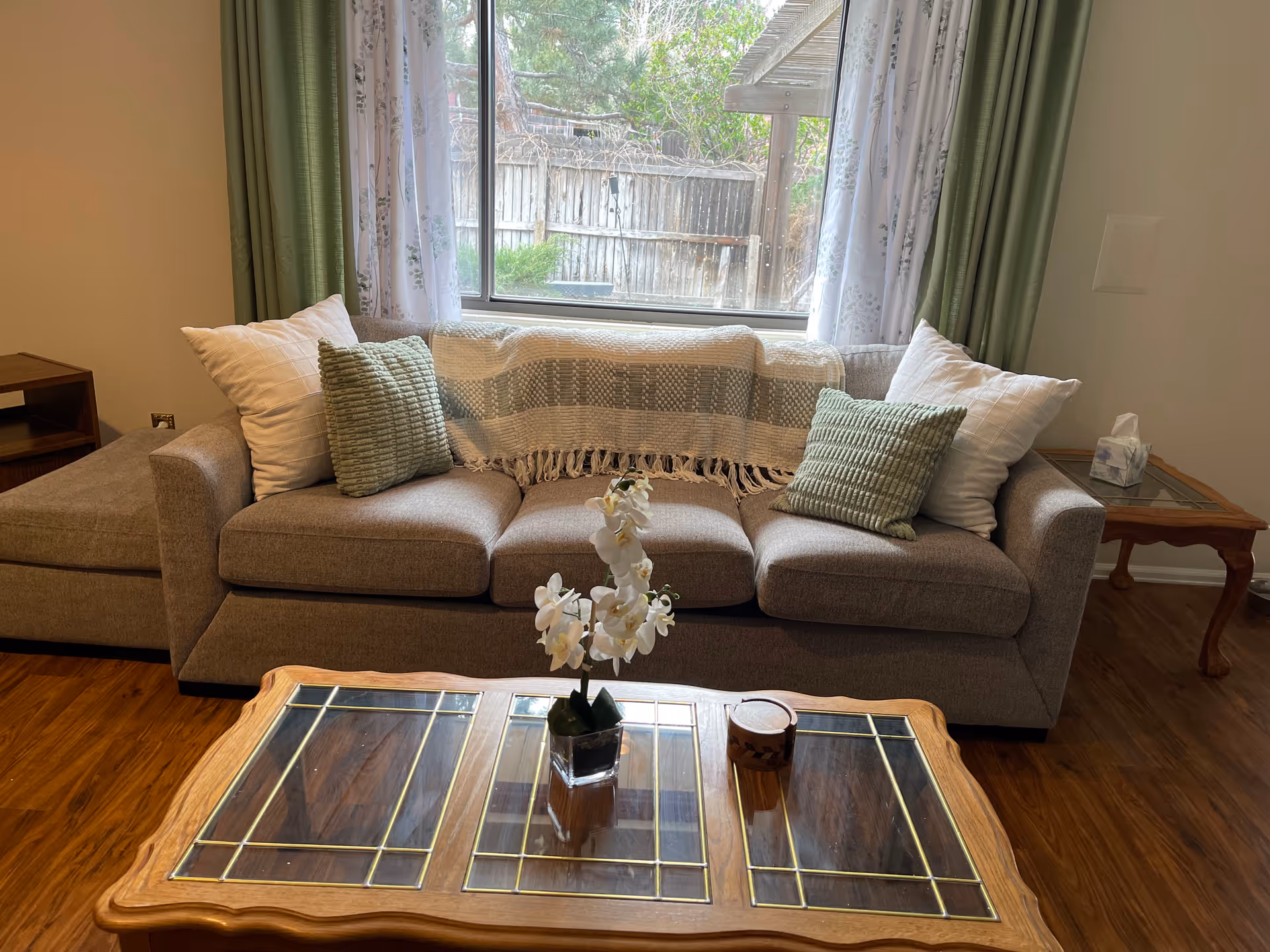 Beige sectional sofa with pillows, throw blanket, and a glass-topped coffee table in a living room.
