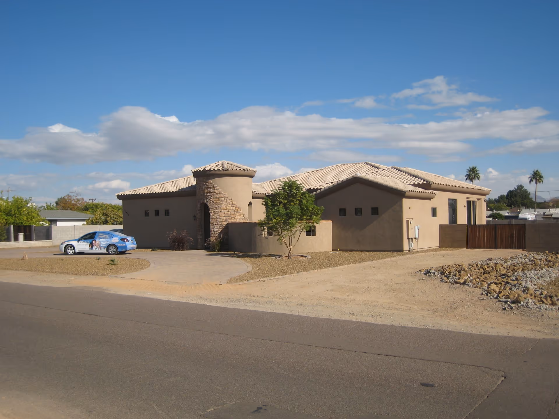 Single-story beige desert-style building with tile roof and curved entry, driveway in arid landscape.