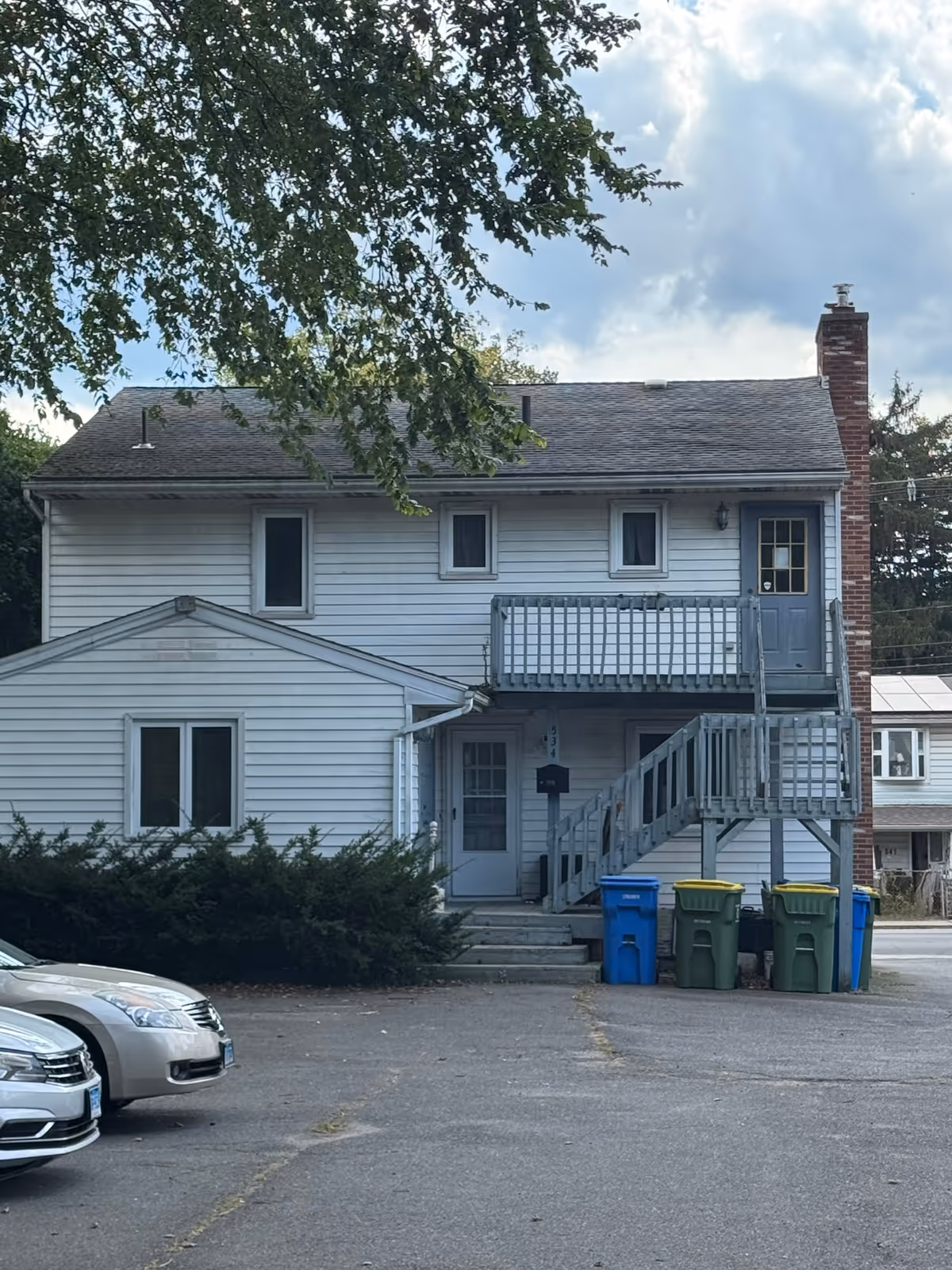 Two-story white building with exterior stairs, balcony, and parked cars in front.