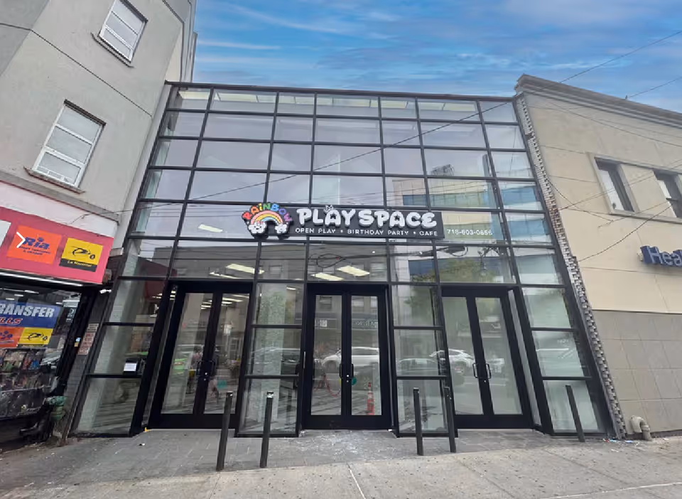 Glass storefront with black-framed windows and a sign 'PlaySpace' on a city street.
