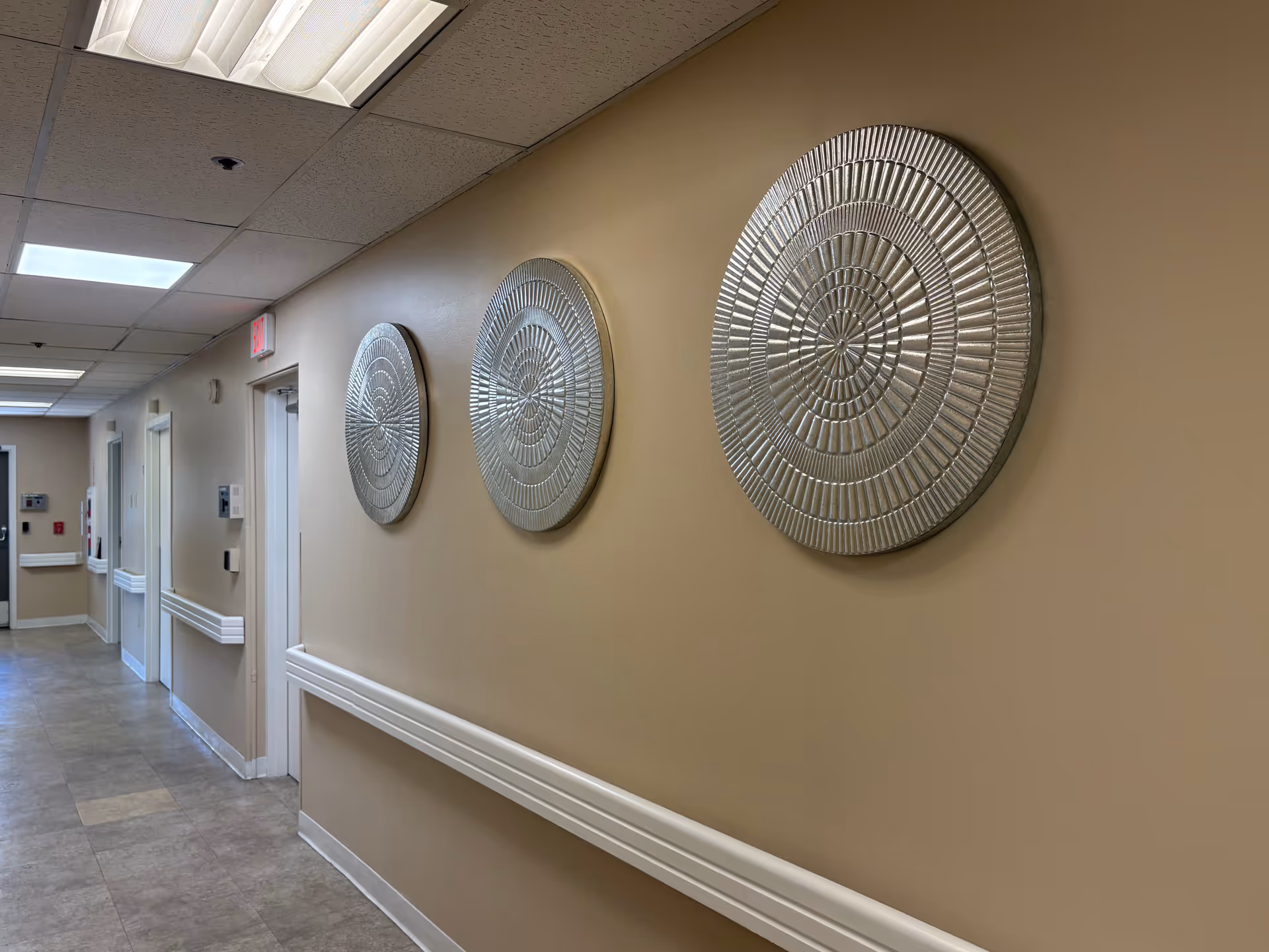 Interior corridor of Bethlehem Manor Memory Care featuring beige walls and three circular metal wall sculptures.