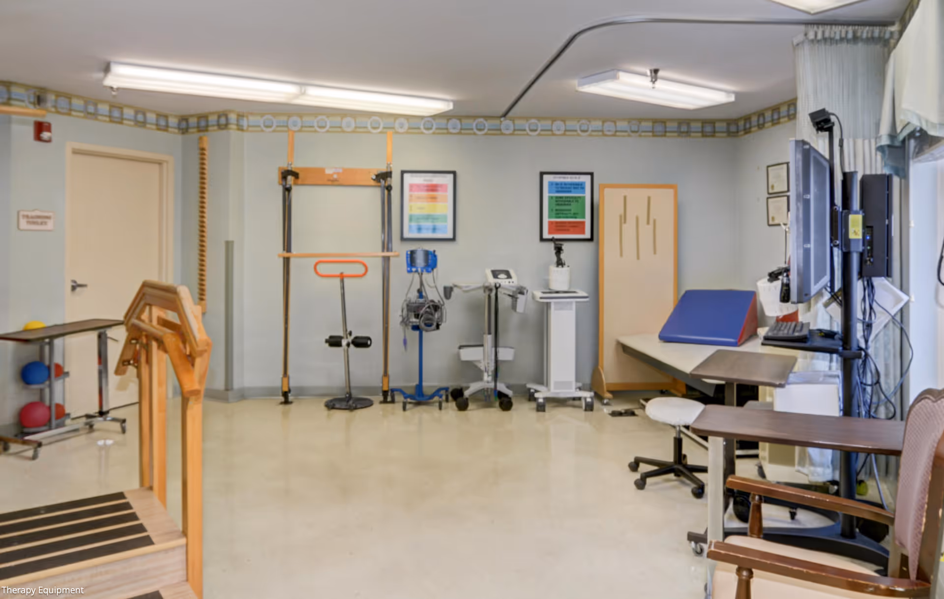 Therapy gym with parallel bars, exercise equipment, and a desk inside a senior facility.