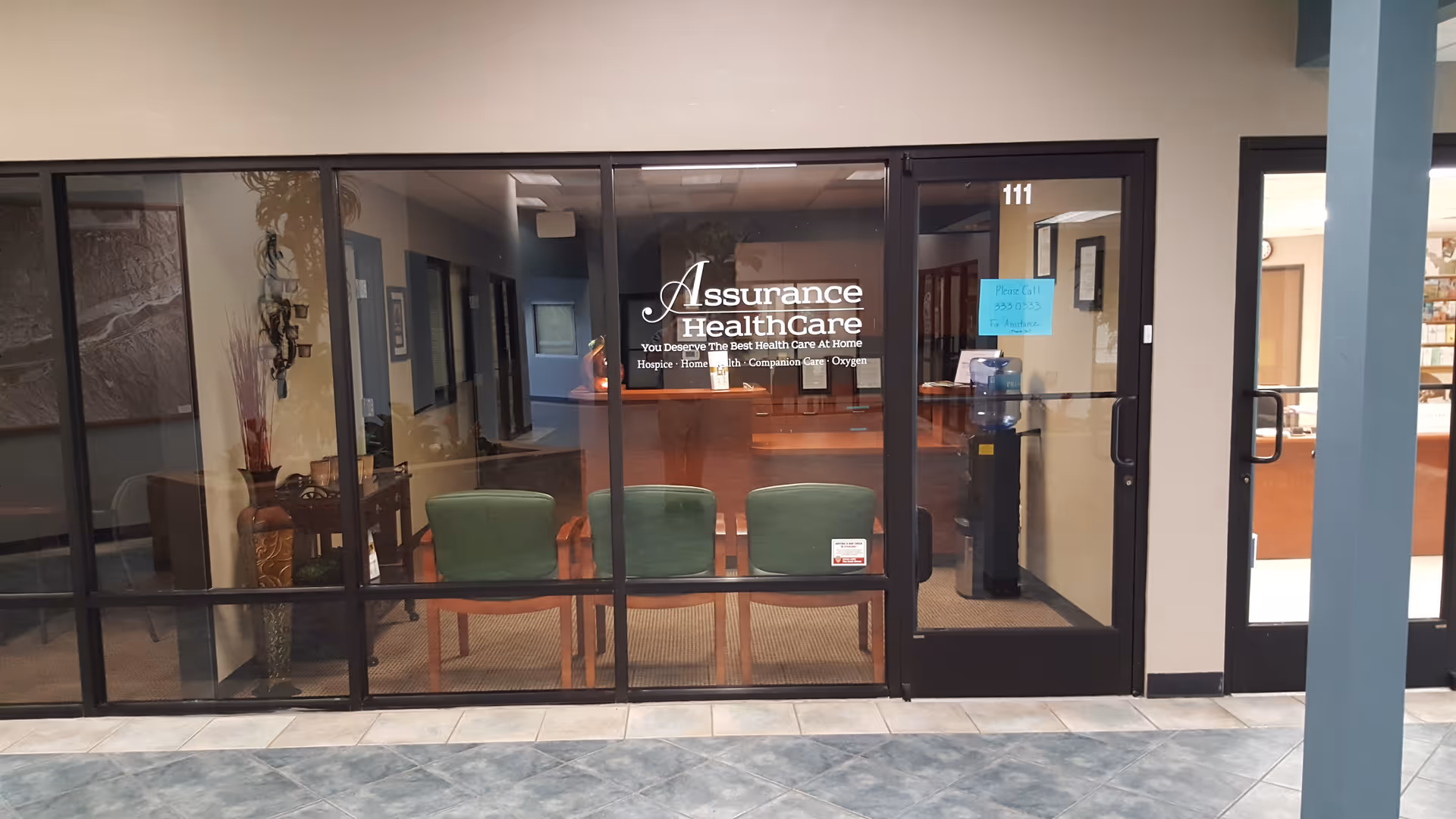 Glass-front entrance to Assurance Health Care with chairs visible inside a lobby.