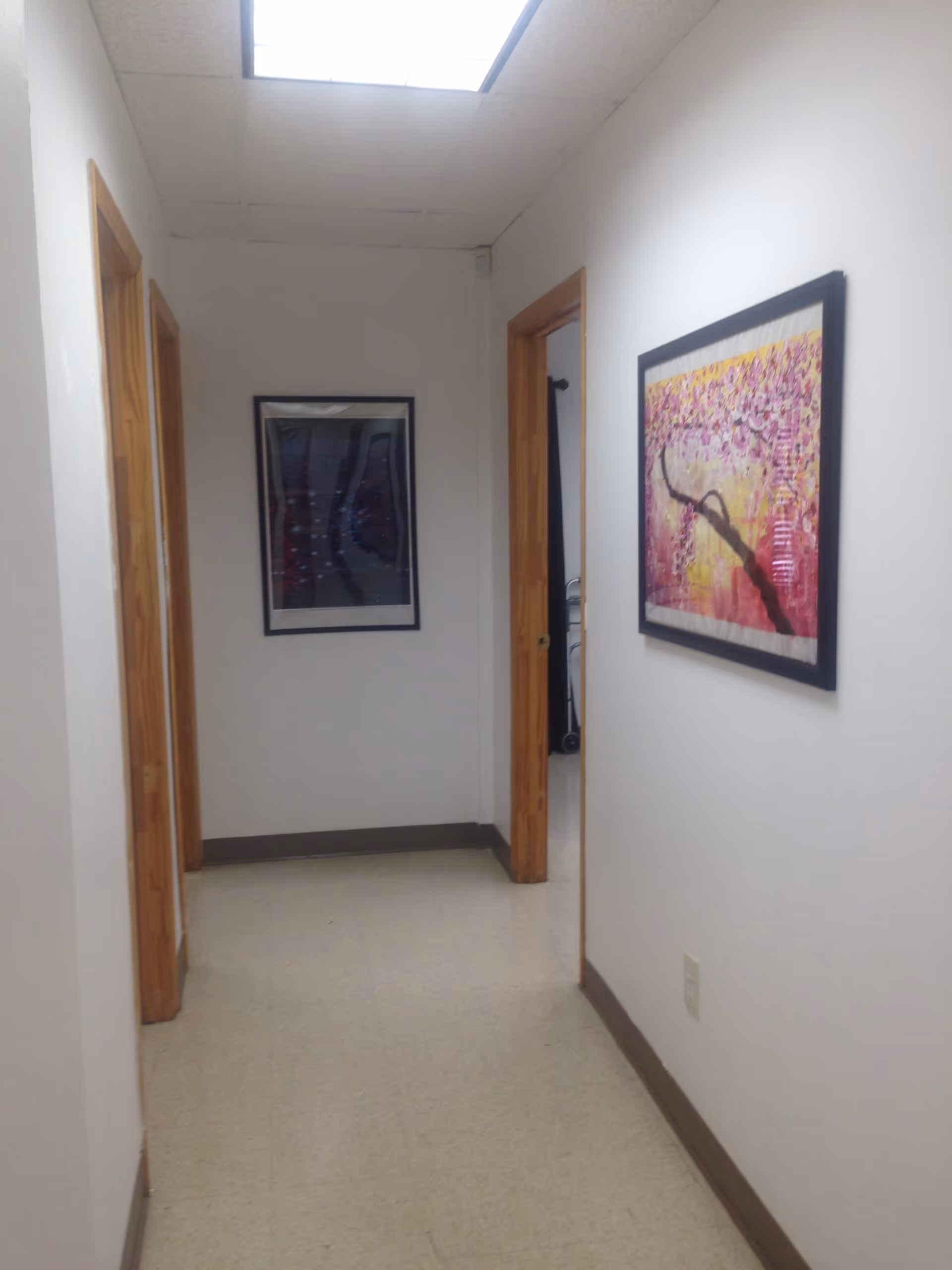 White hallway with framed artwork and open doorways along walls.