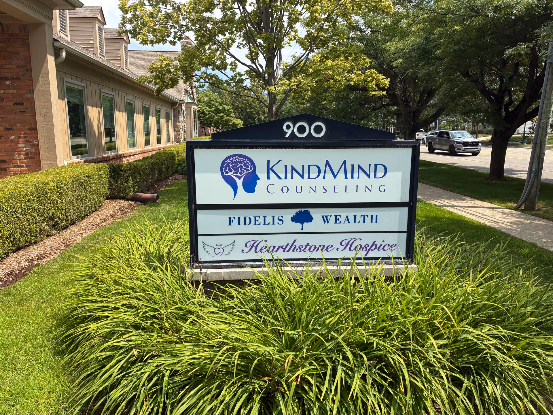 Exterior sign displays Hearthstone Hospice with KindMind Counseling and Fidelis Wealth in front of building.