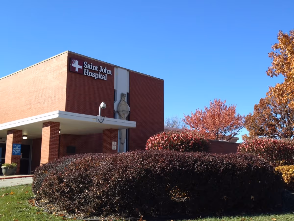Brick hospital building with Saint John Hospital sign, entrance canopy, and autumn trees.