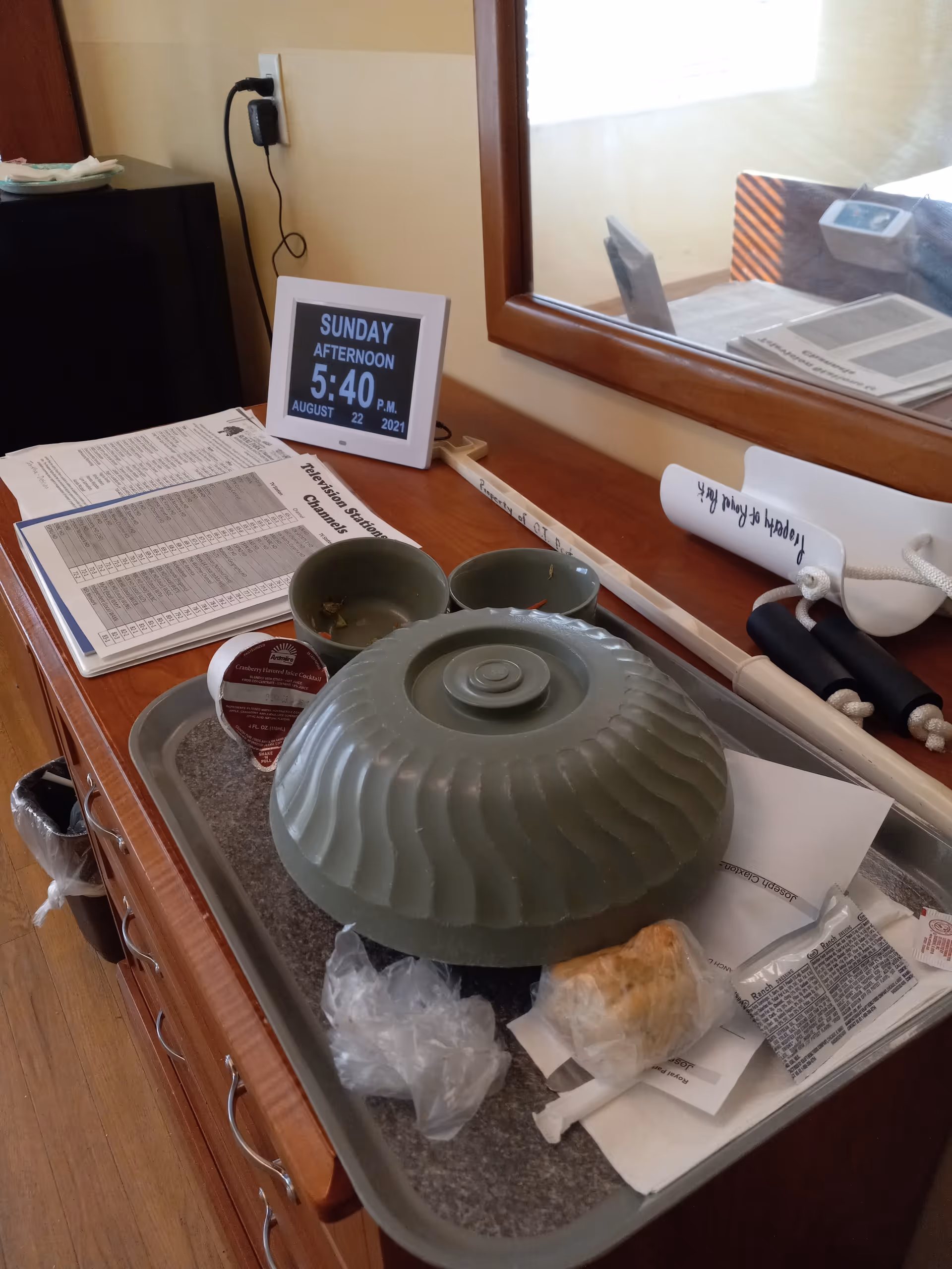Desk in a resident room with a tray, clock, papers, and a gray ribbed cloche.