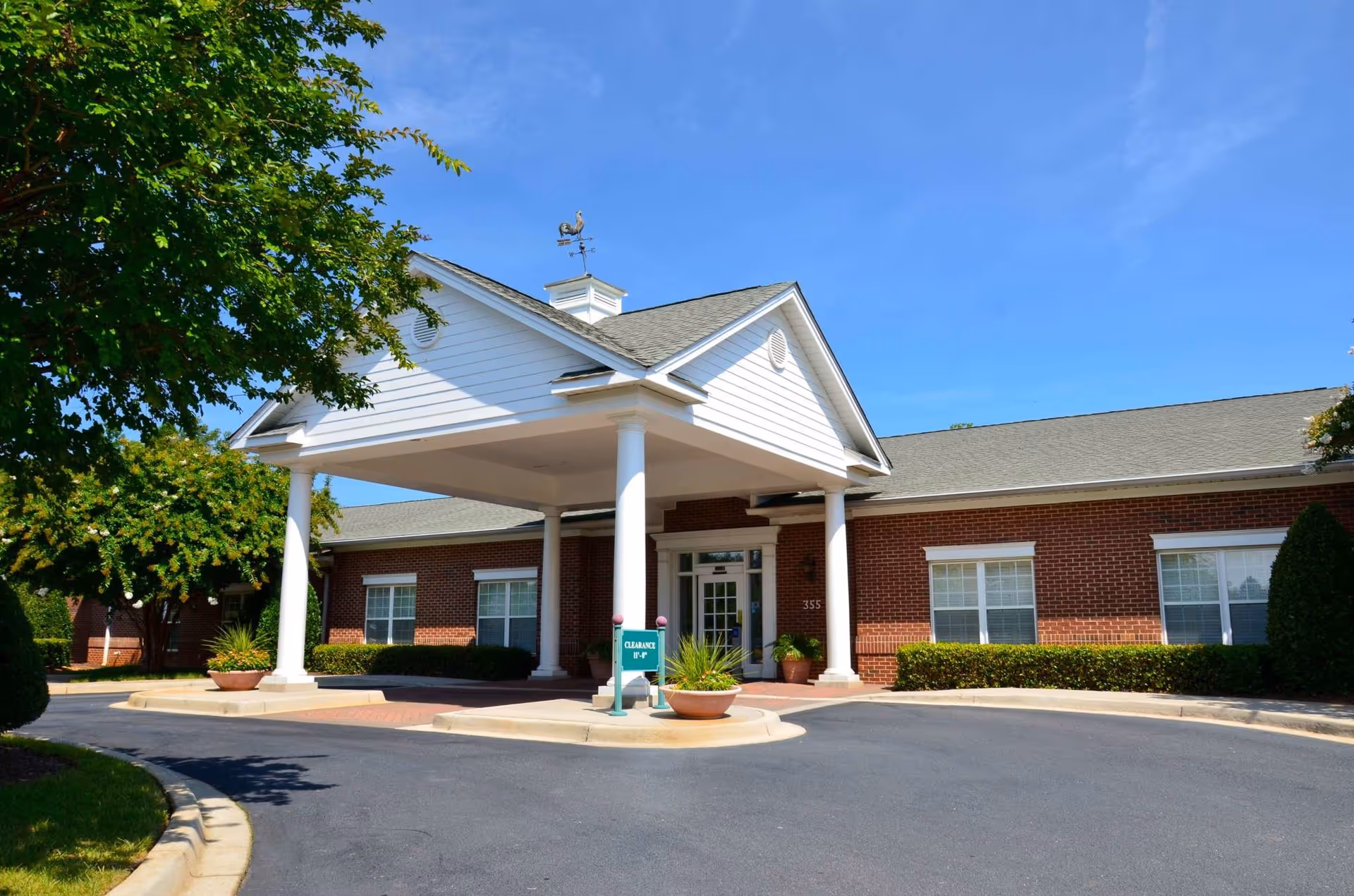 Brick senior living facility with a white portico entrance and landscaped driveway.