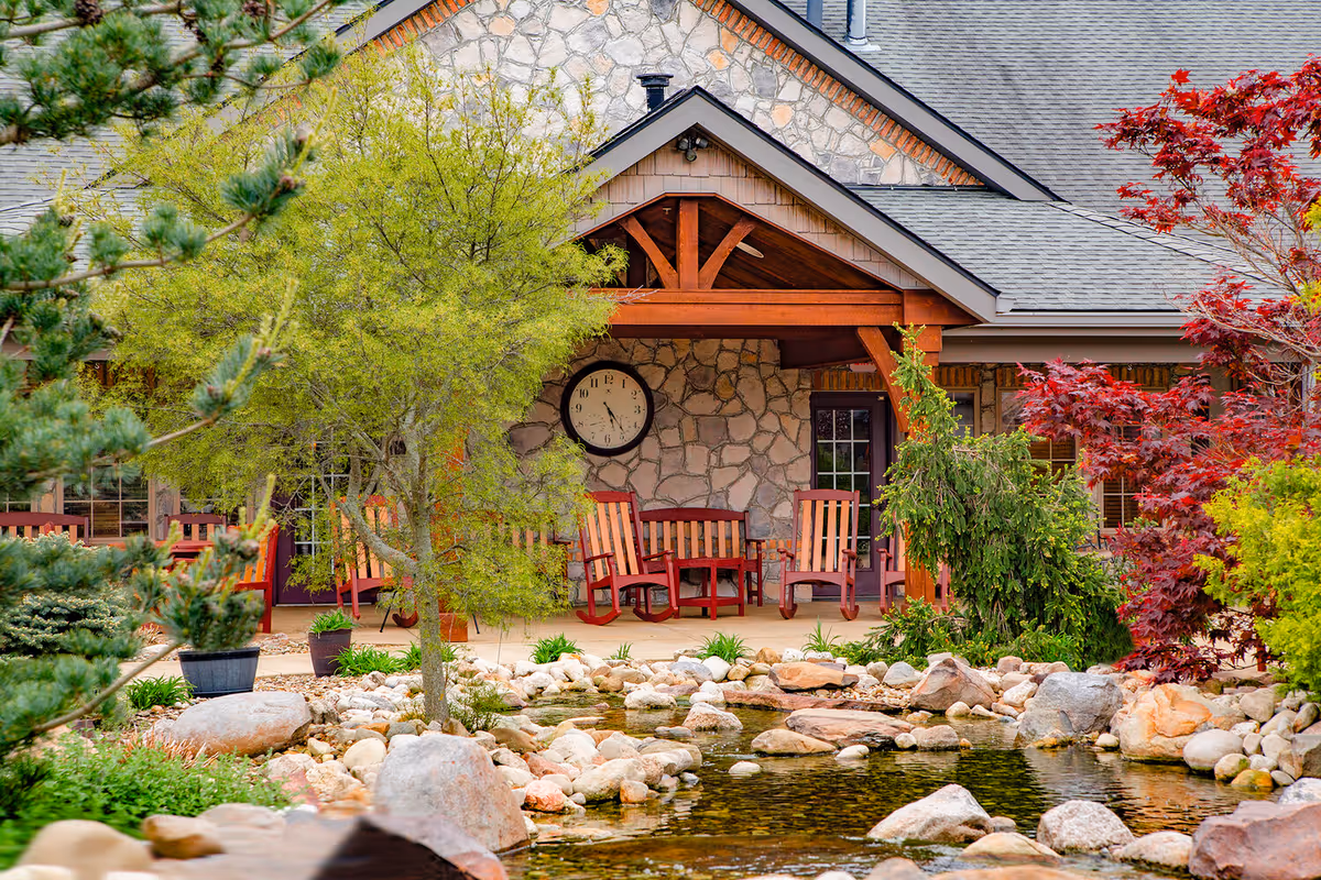 Stone building with a wooden porch, several red chairs, and a landscaped rock pond.
