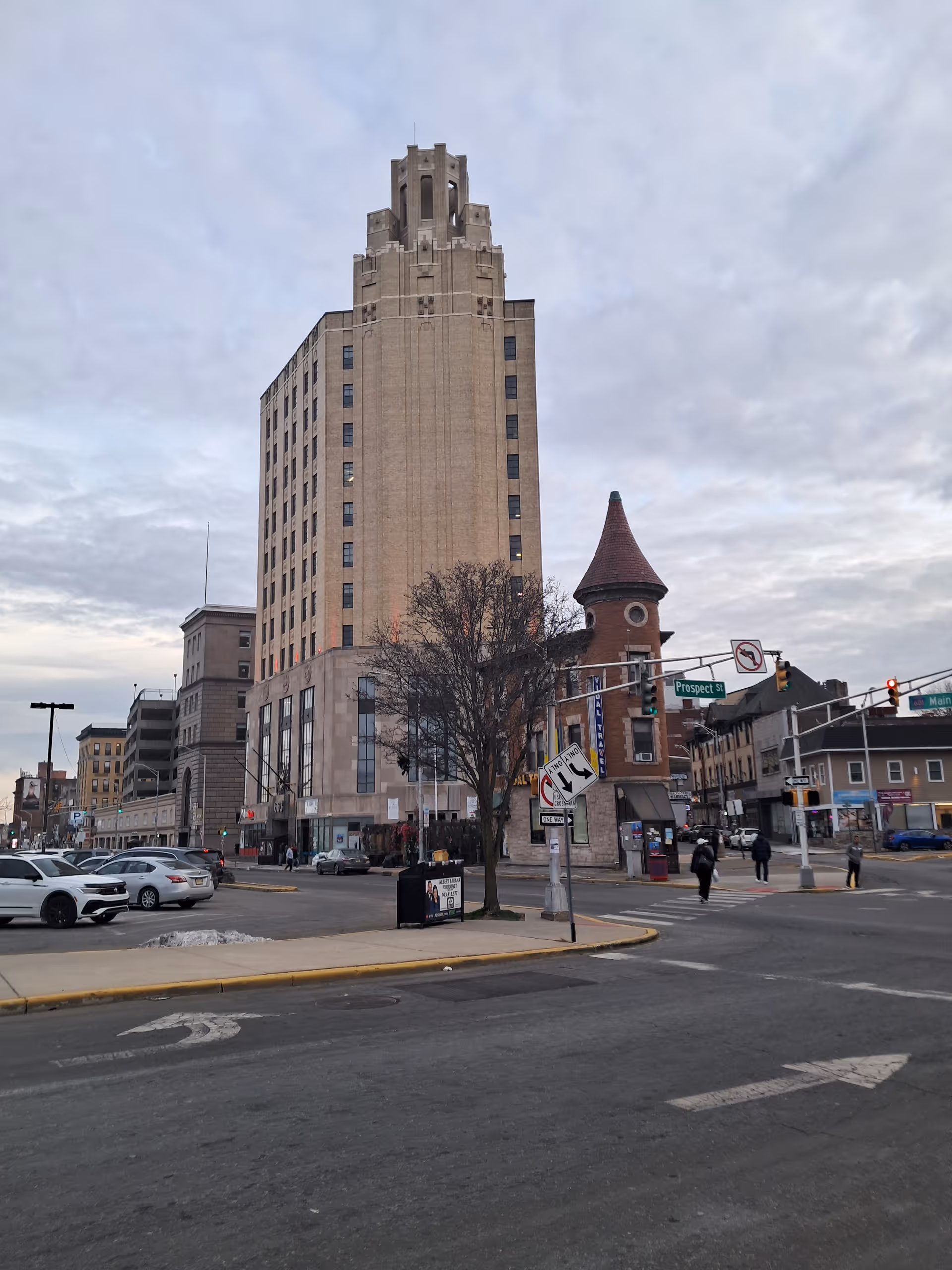 Urban street scene with a tall beige building and a turreted structure at an intersection.