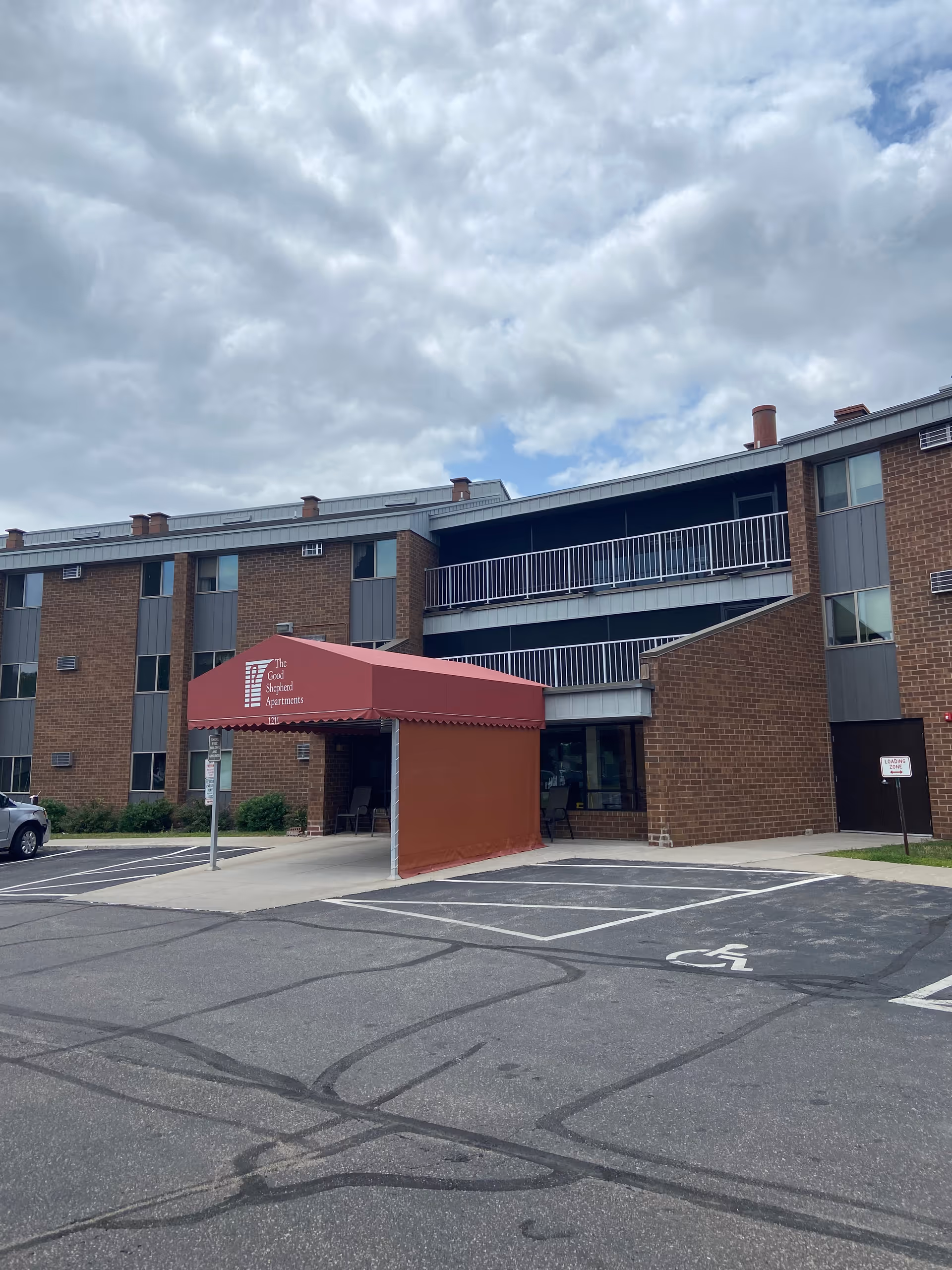 Brick building exterior with a maroon entrance canopy and adjacent parking lot.