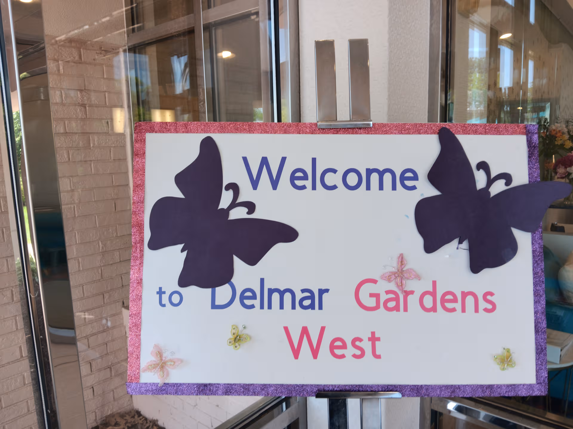 Welcome to Delmar Gardens West sign with purple butterflies at facility entrance
