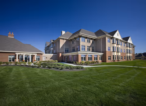 A large multi-story senior living facility with well-kept lawn and blue sky.