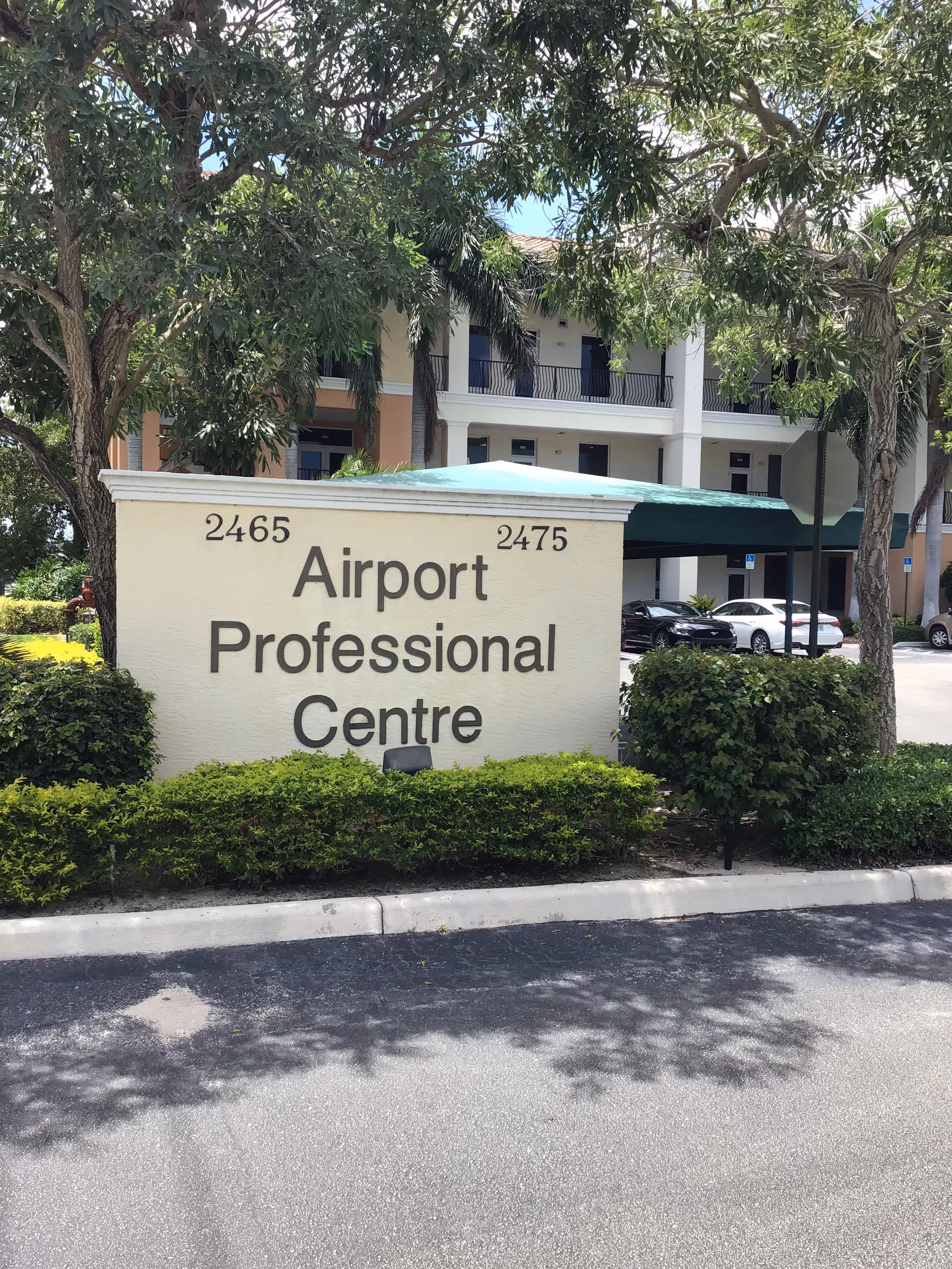 Outdoor sign for Airport Professional Centre with a building and greenery in the background.