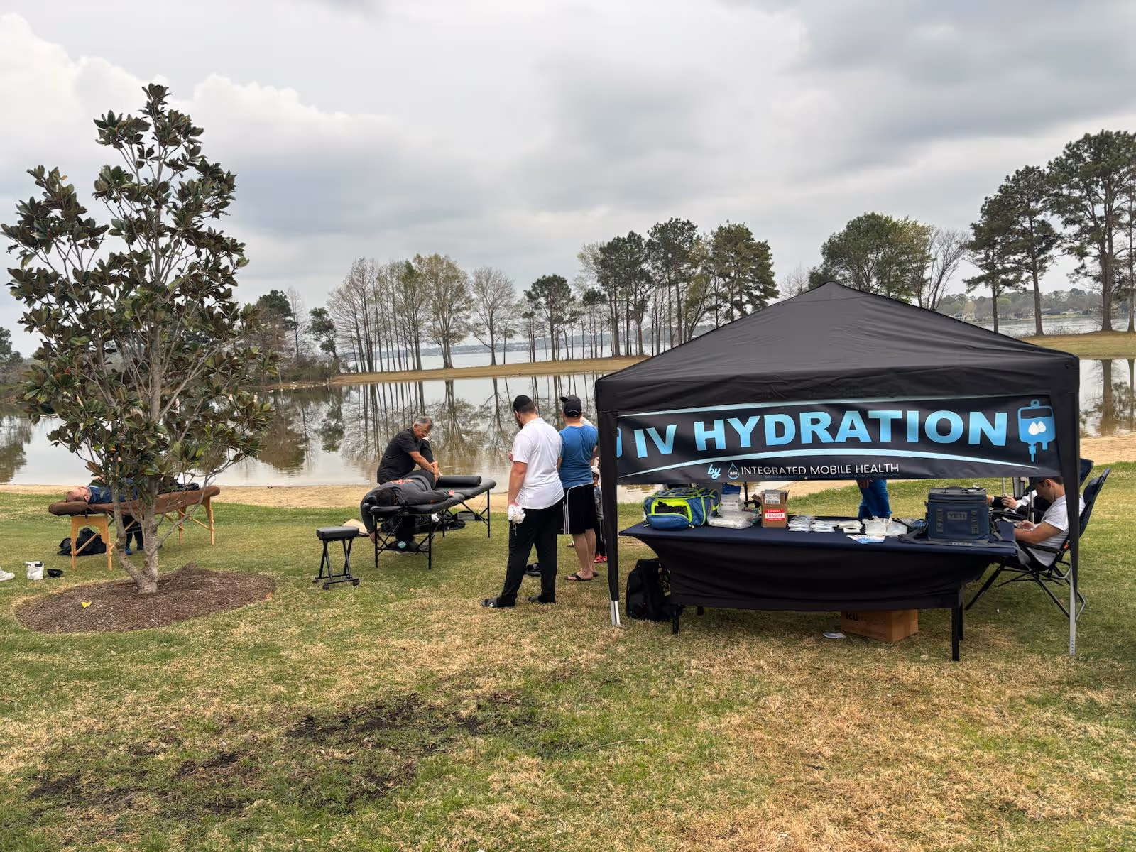 Outdoor lakeside setup with a black tent labeled LIV HYDRATION and people around