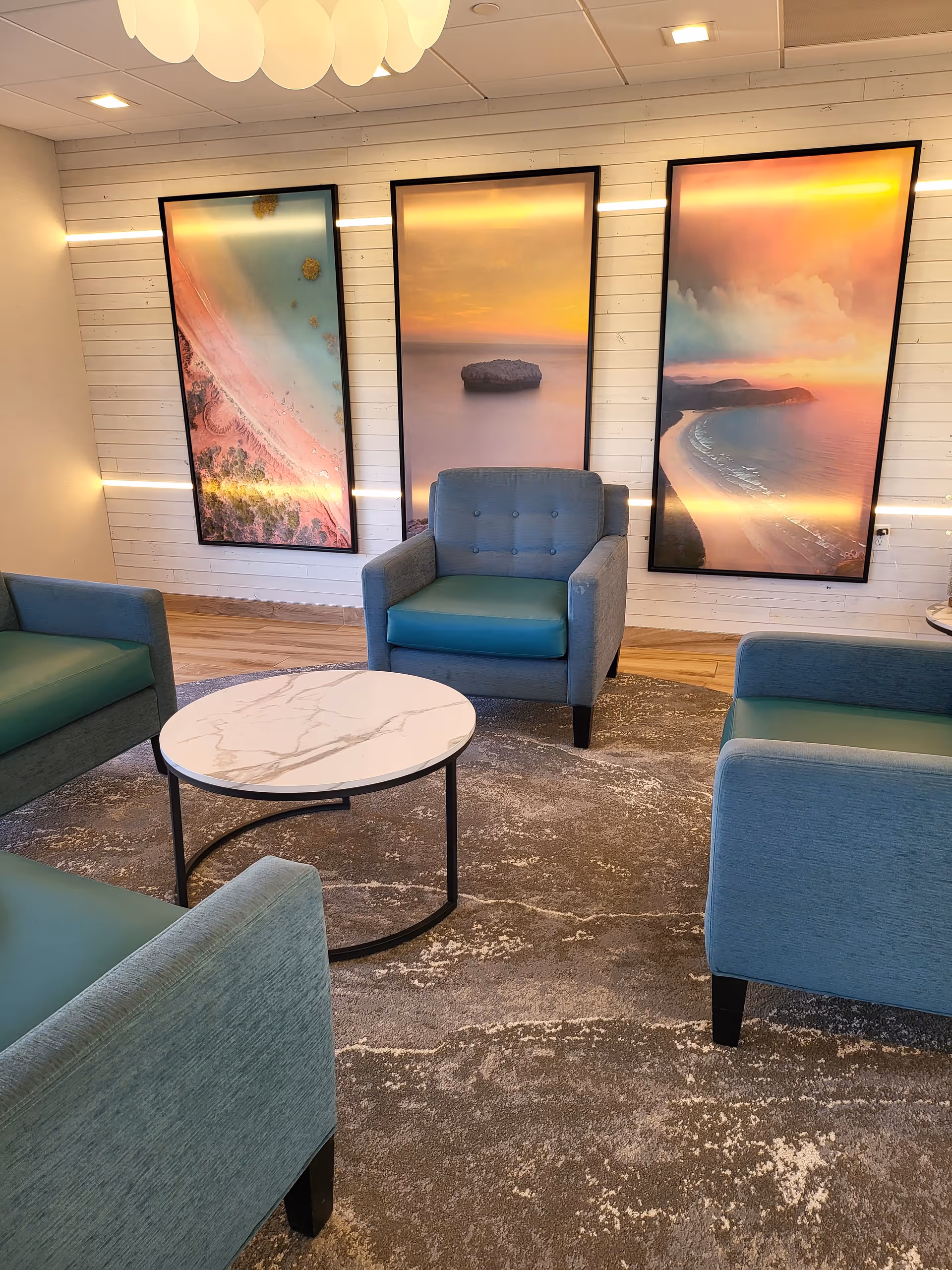 Bright lobby seating area with blue chairs, a round marble table, and large wall art.