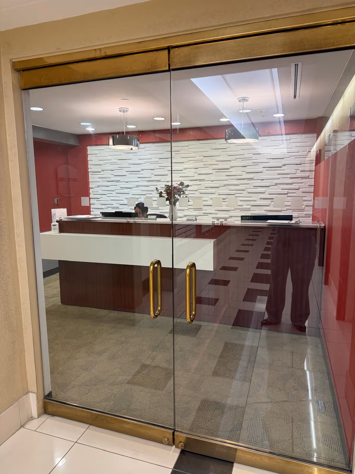 Glass entry doors reveal a modern lobby with a reception desk and textured wall.