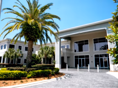Exterior view of a modern medical facility entrance with palm trees and blue sky.