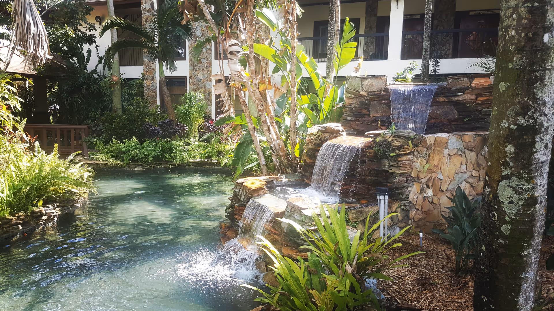 Lush outdoor courtyard with cascading rock waterfall, pool, and tropical plants.