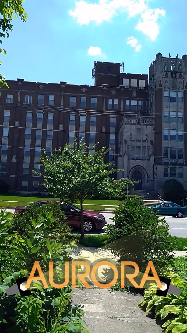 Front view of a large brick building with landscaped greenery and a sidewalk.