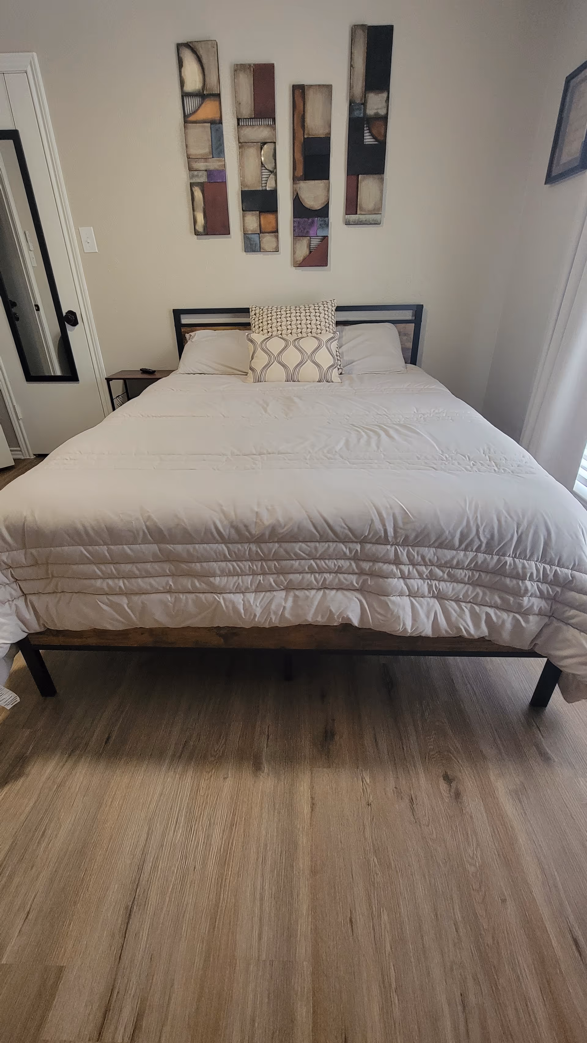 A neatly made bed with decorative pillows in a small, neutral-toned bedroom.