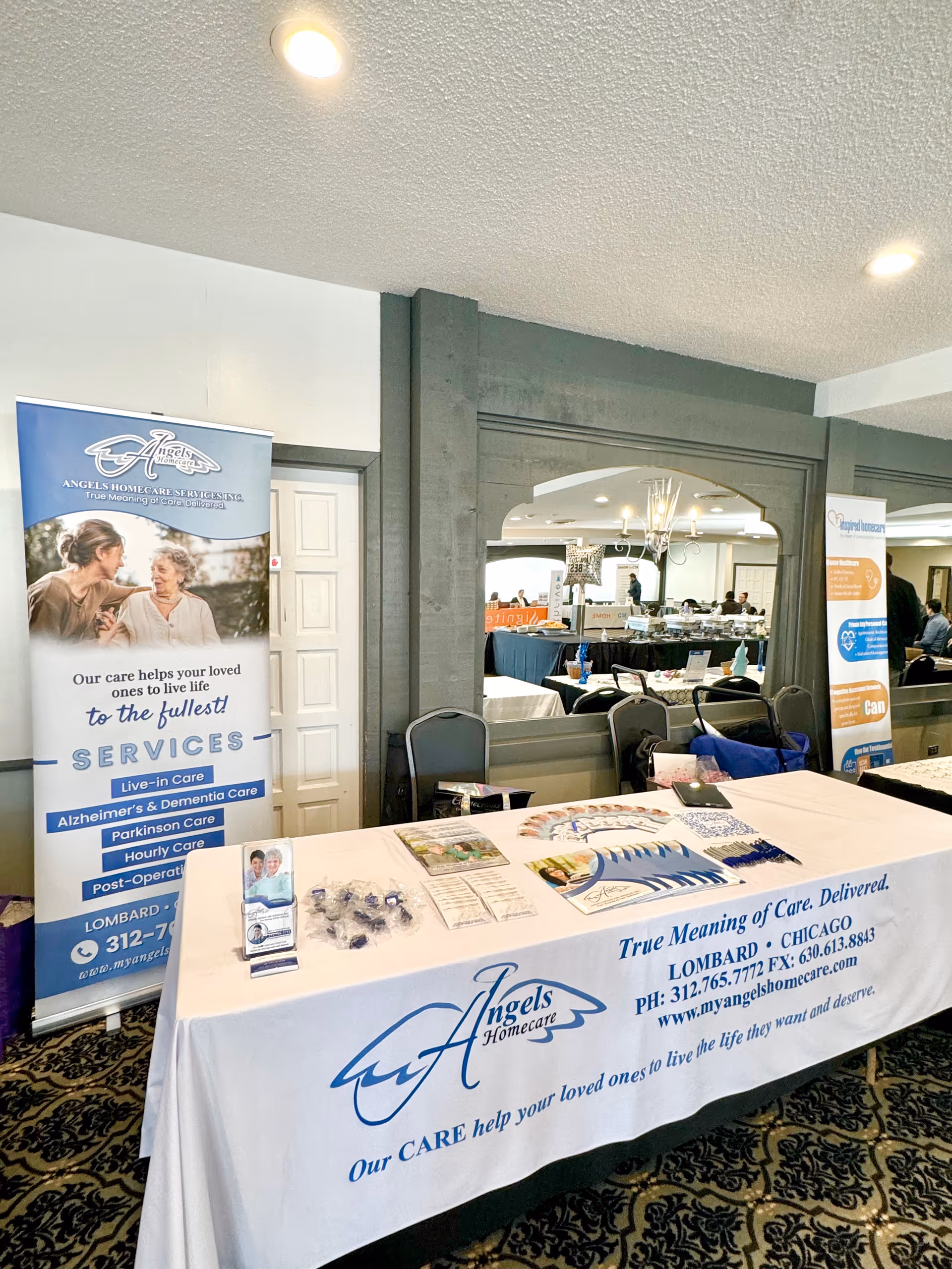 Indoor expo booth for Angels Homecare with banners, a table, and promotional materials.