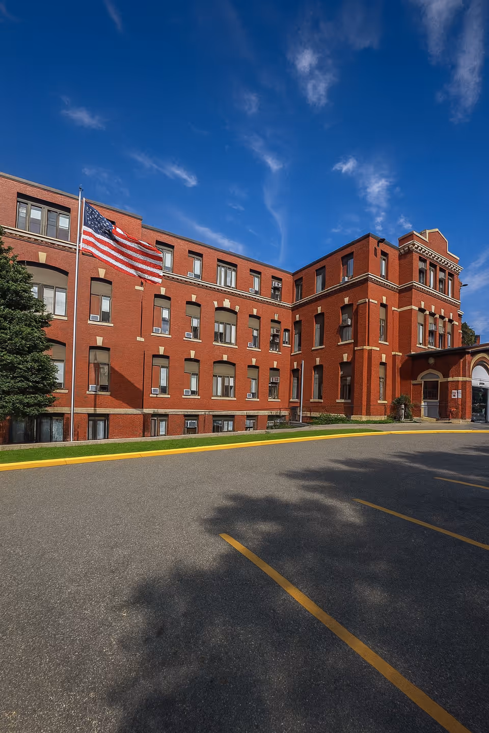 Red brick multi-story building with American flag on a flagpole against a blue sky.